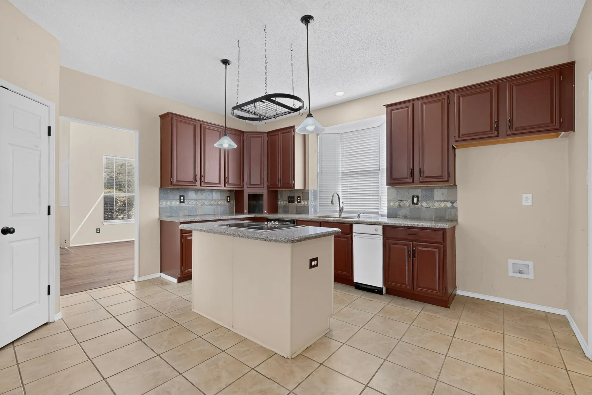 Spacious kitchen featuring rich wood cabinetry, a large center island with seating space, stainless steel appliances including a dishwasher, tile flooring throughout, and abundant natural light from multiple windows
