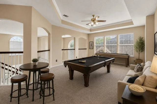 Staged Spacious loft area featuring a tray ceiling, multiple windows, archways, and carpeted flooring