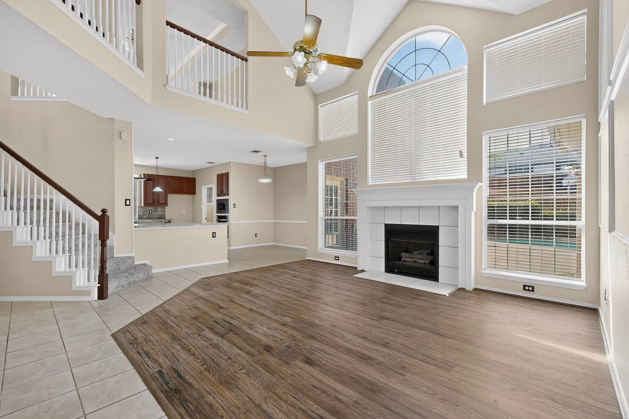 Spacious living area featuring wood-finish flooring, a white fireplace with a tile surround, and an arched window
