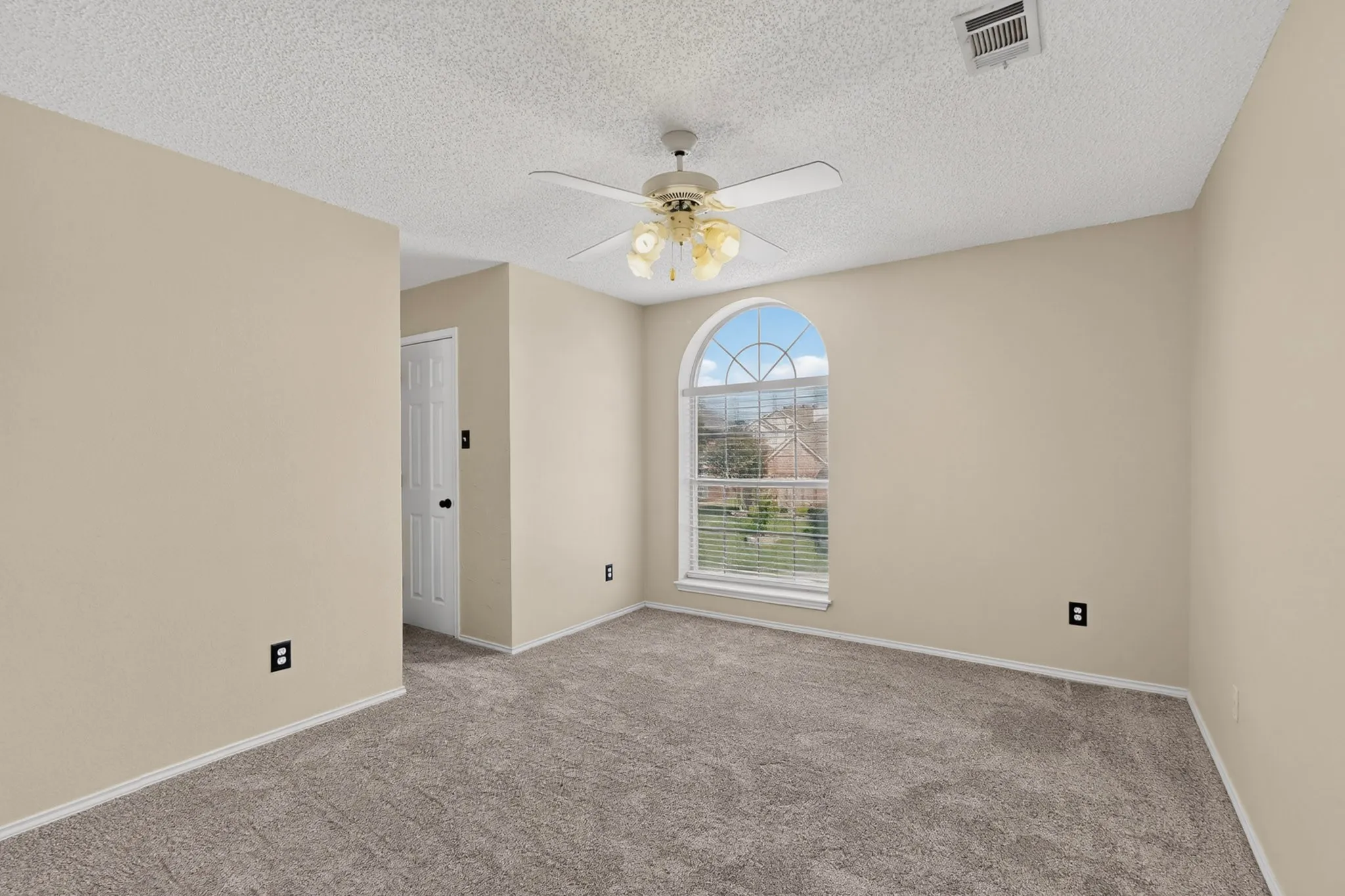 Carpeted room featuring an arched window, a ceiling fan with integrated lighting, a recessed air vent, and neutral wall paint