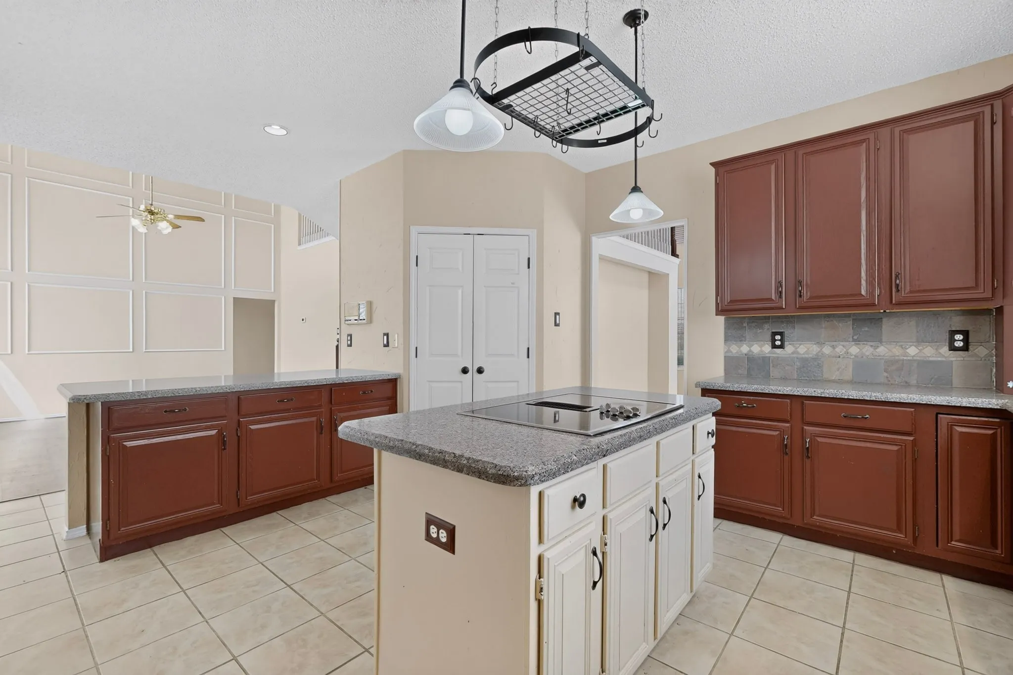 Kitchen featuring an island cooktop, granite-style countertops, wood-finish cabinetry, tile flooring, and a decorative pot rack