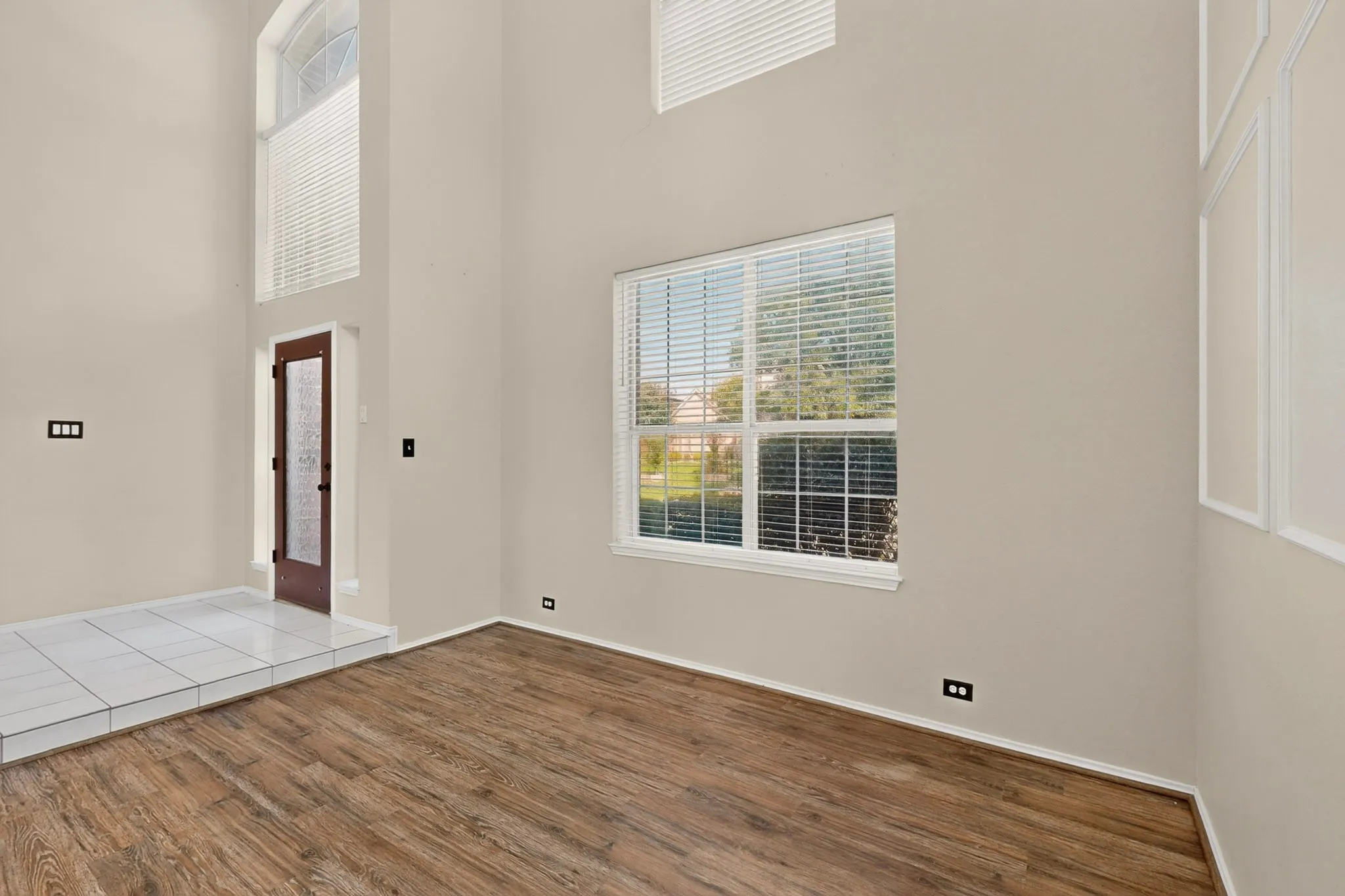 Two-story entry foyer featuring a dark wood-finish door with frosted glass, transom window, and white tile flooring