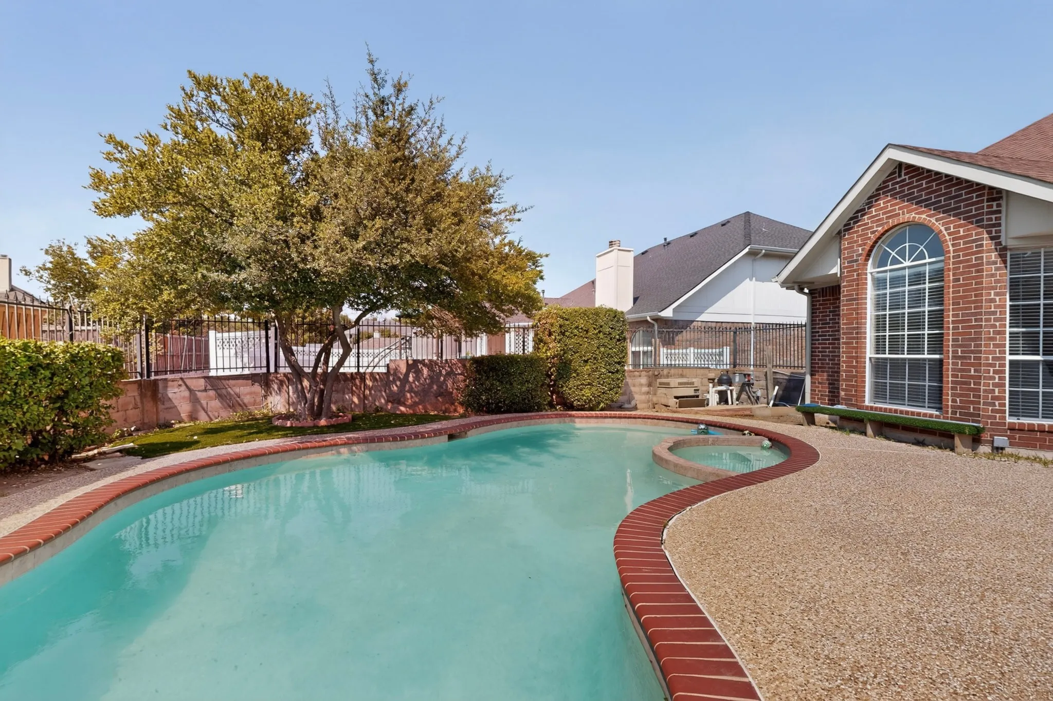 Curved swimming pool with integrated spa, bordered by a textured aggregate deck and brick coping