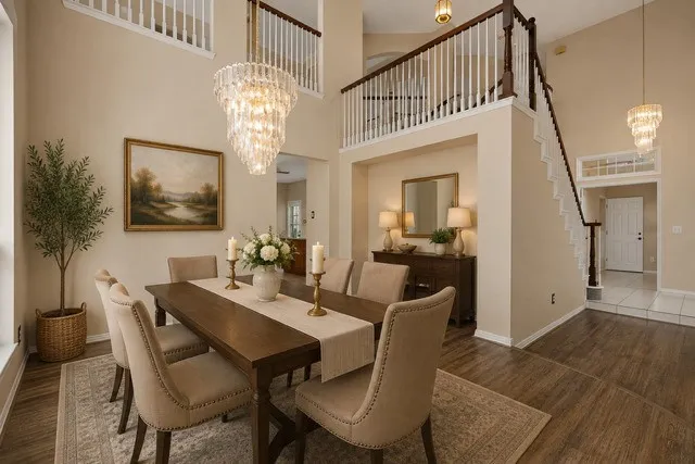 Staged Elegant dining room showcasing a wood-finish dining table, upholstered chairs with nailhead trim, and soaring two-story ceilings with a crystal chandelier