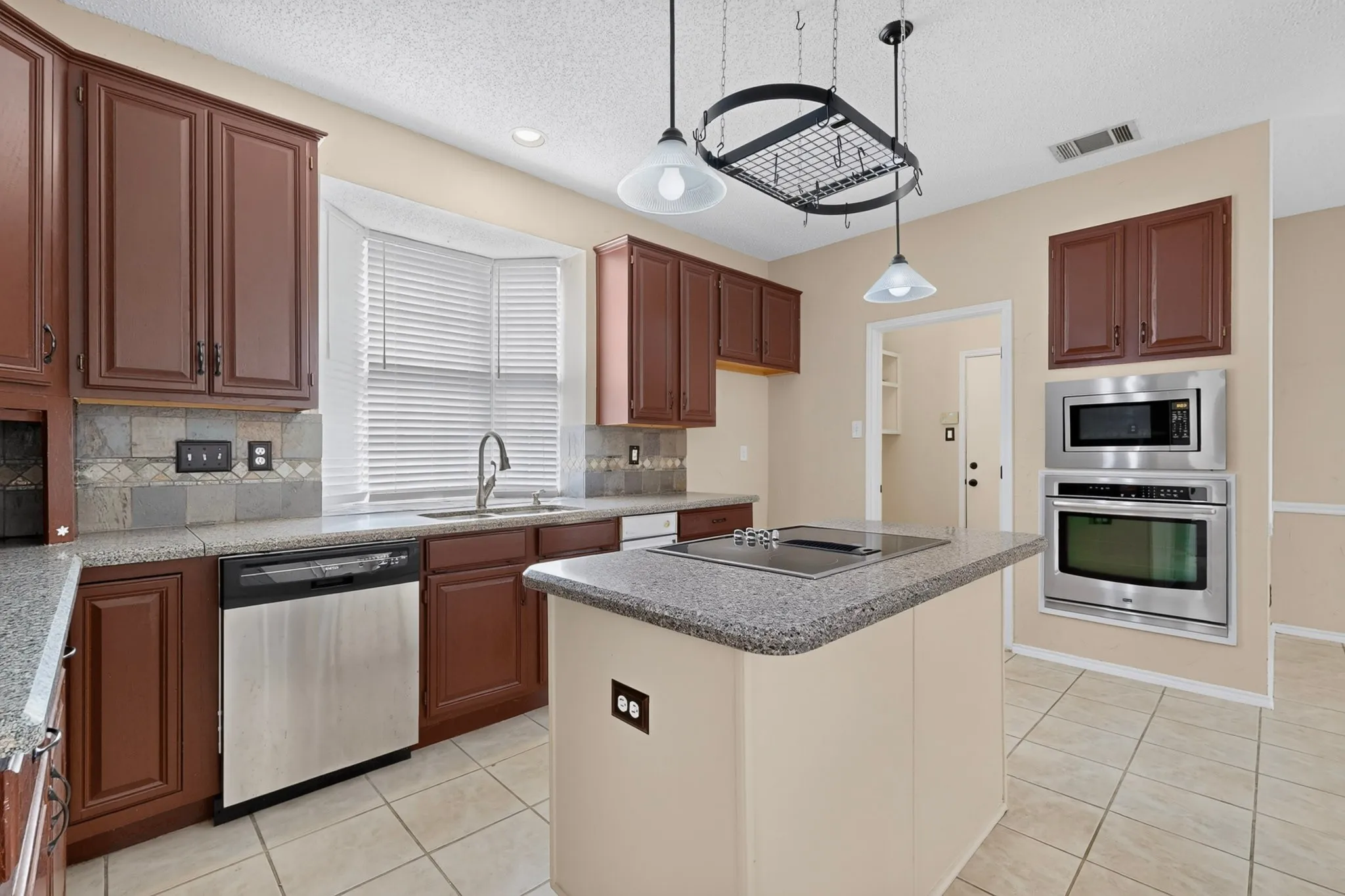 Kitchen featuring a center island with built-in cooktop, stainless steel appliances, dark wood cabinetry, tile flooring, and a bay window