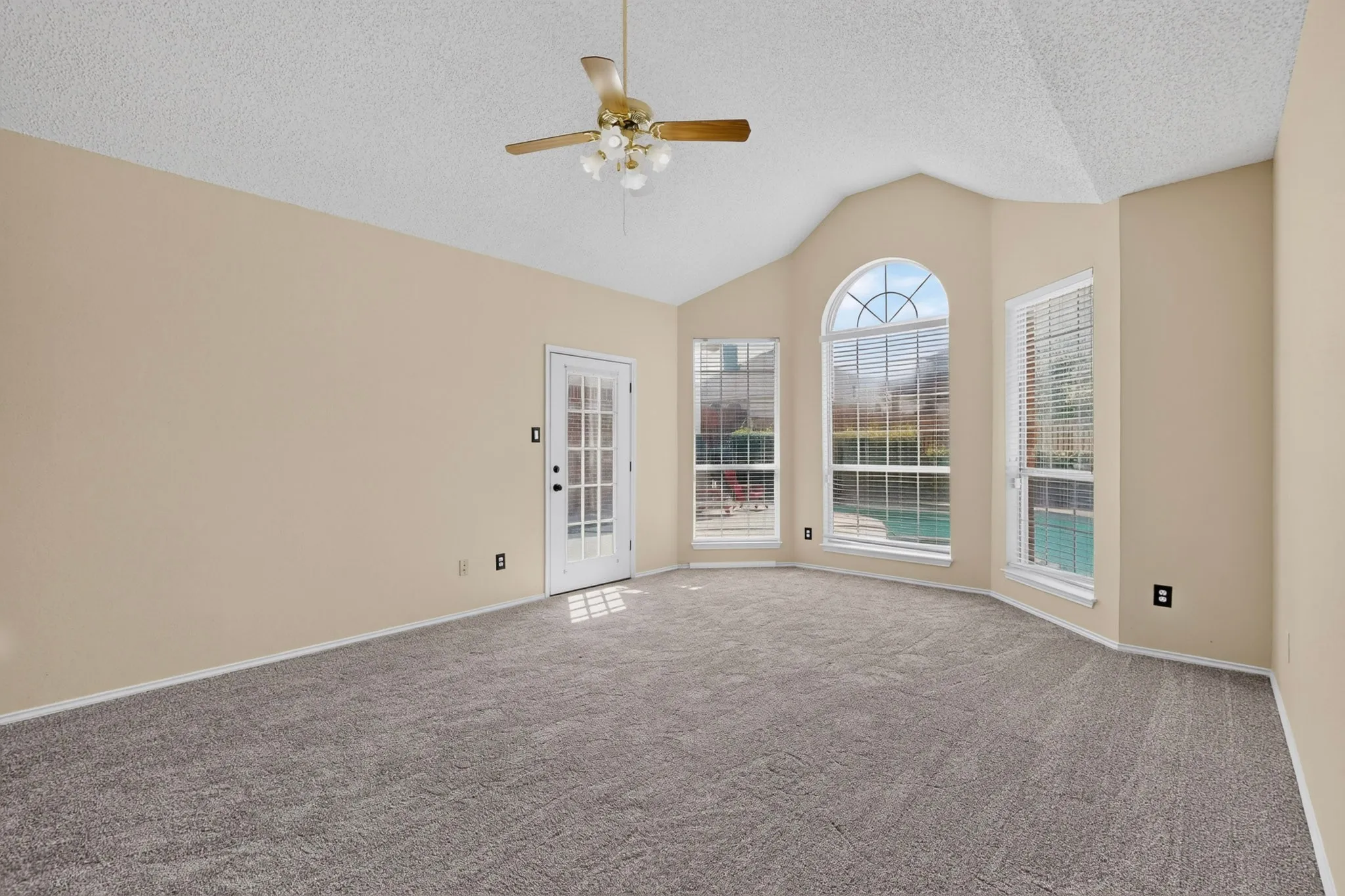 Vaulted ceiling room featuring a decorative ceiling fan, light beige wall color, and gray patterned carpeting