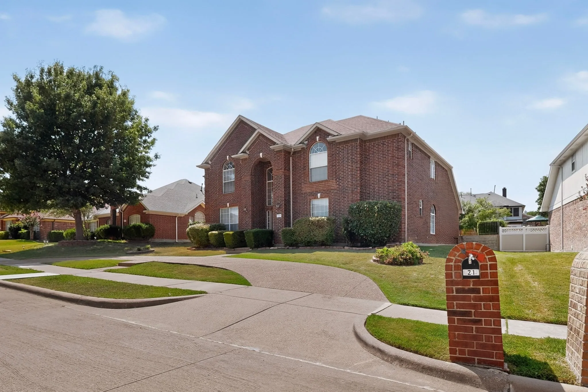 Traditional brick exterior featuring arched windows, mature landscaping, and a substantial driveway
