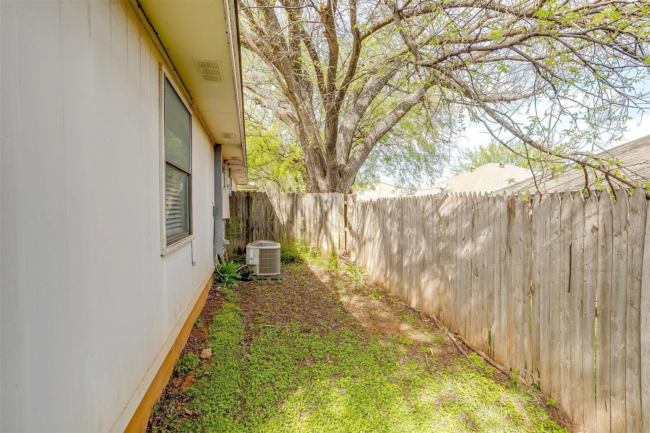 Side yard featuring a wooden privacy fence and mature tree for shade.
