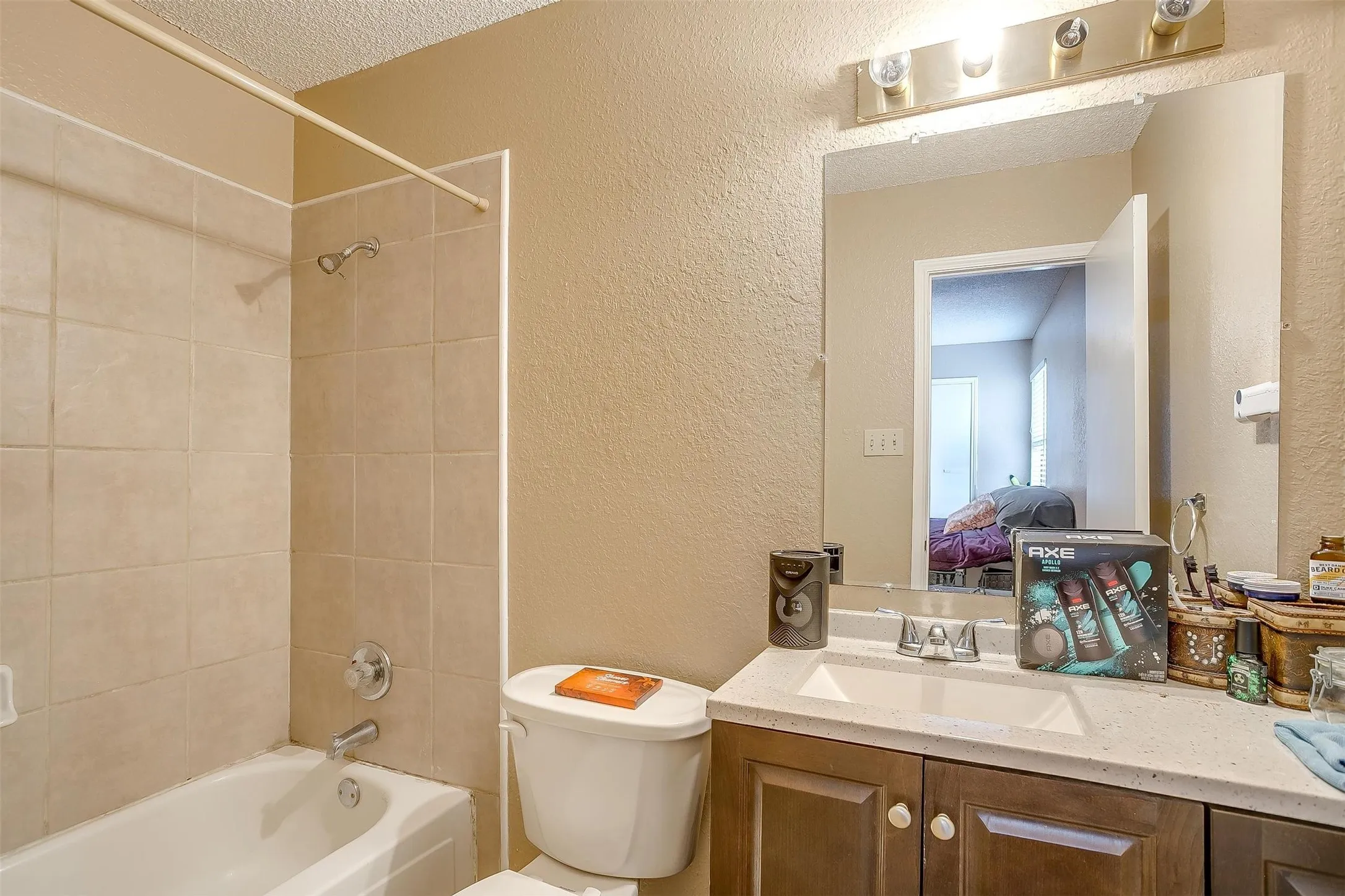 Bathroom featuring textured walls with neutral paint, light colored ceramic tiles lining the shower/tub combination.