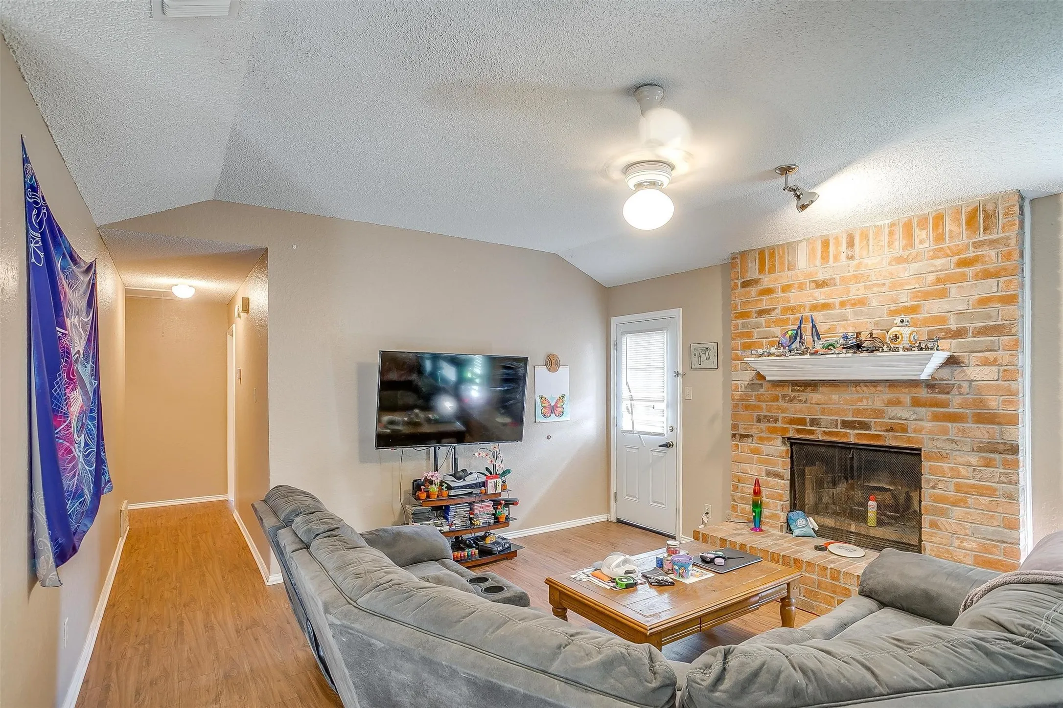 Living room featuring natural wood-like flooring throughout and a large accent wall with fireplace white mantle.