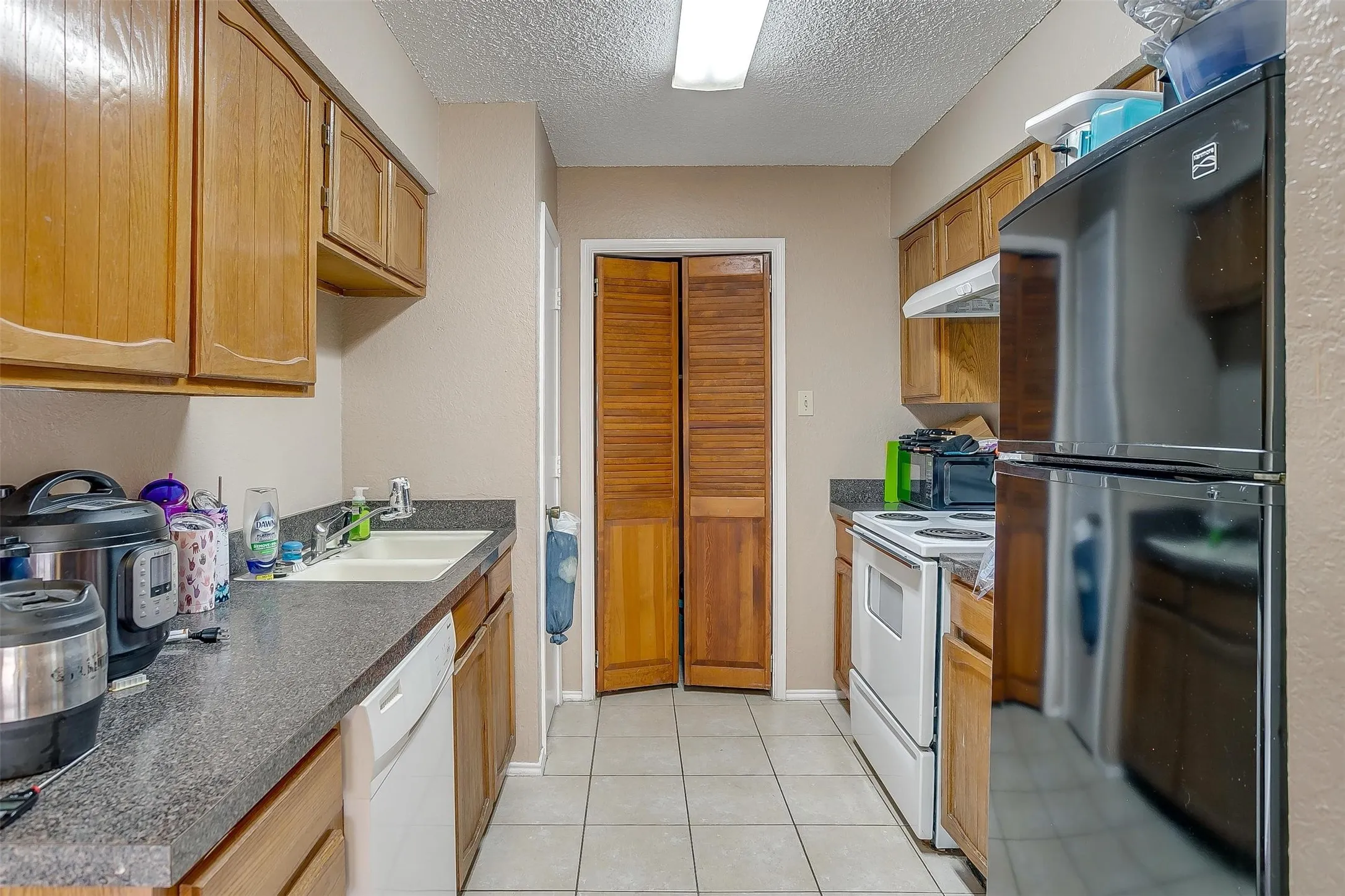 Kitchen featuring galley layout, wood cabinetry, contrasting darker countertops and wooden louvered laundry door.