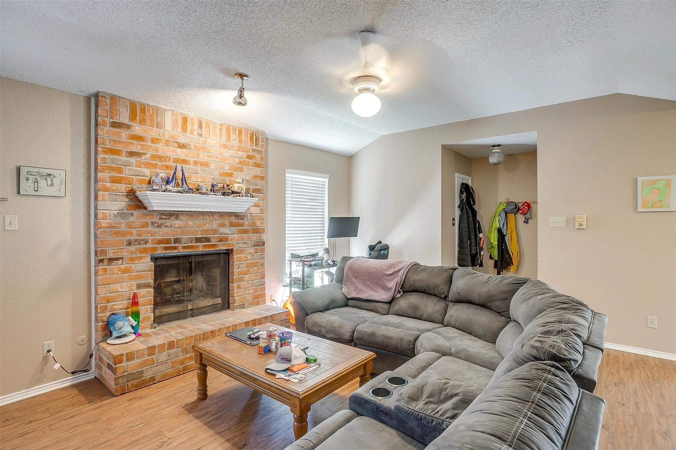 Living room featuring accent wall with brick fireplace with white mantel floorplan that accommodates ample seating.