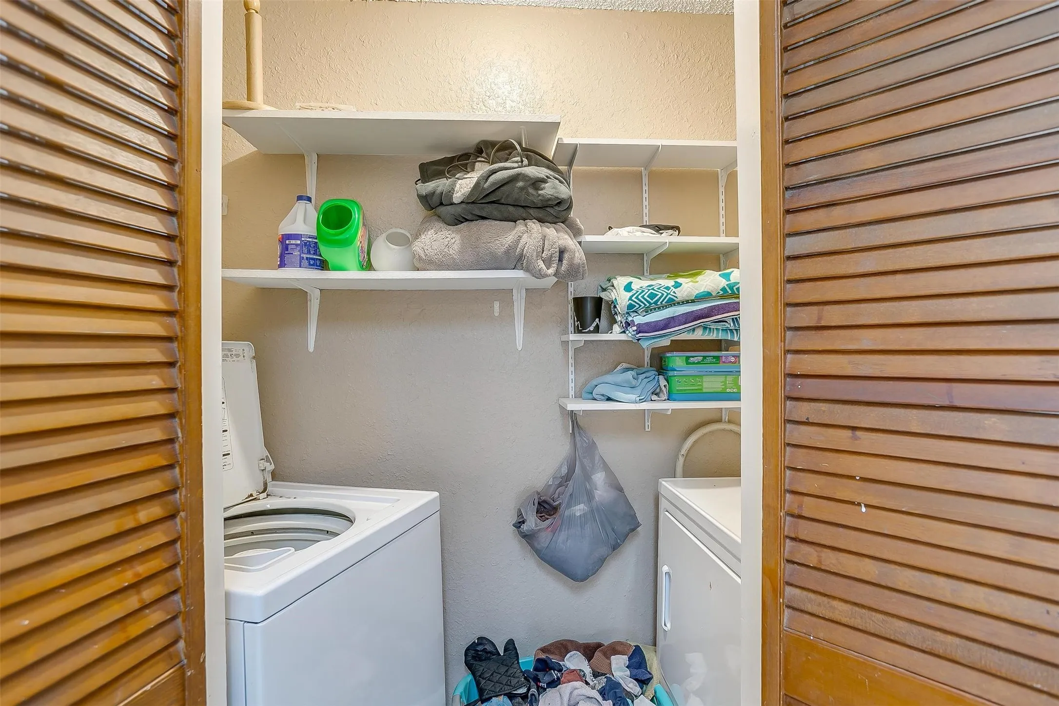 Laundry area featuring slatted wooden doors, with white metal shelving installed on the back wall for organized storage.
