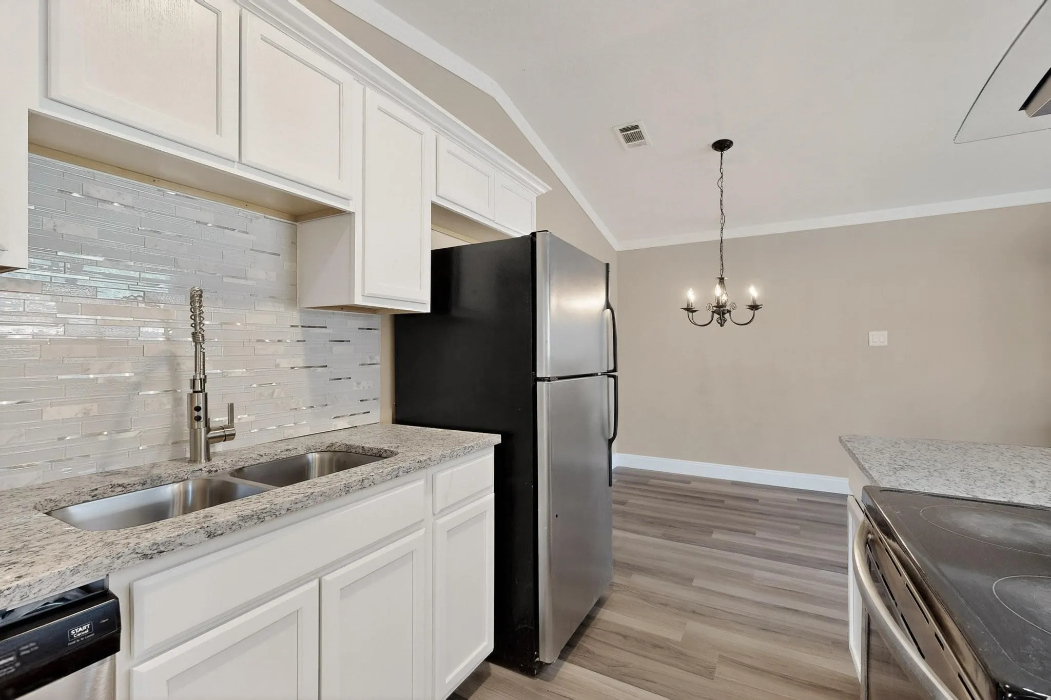 Kitchen featuring backsplash, white cabinetry, light stone countertops, crown molding, and light wood-type flooring