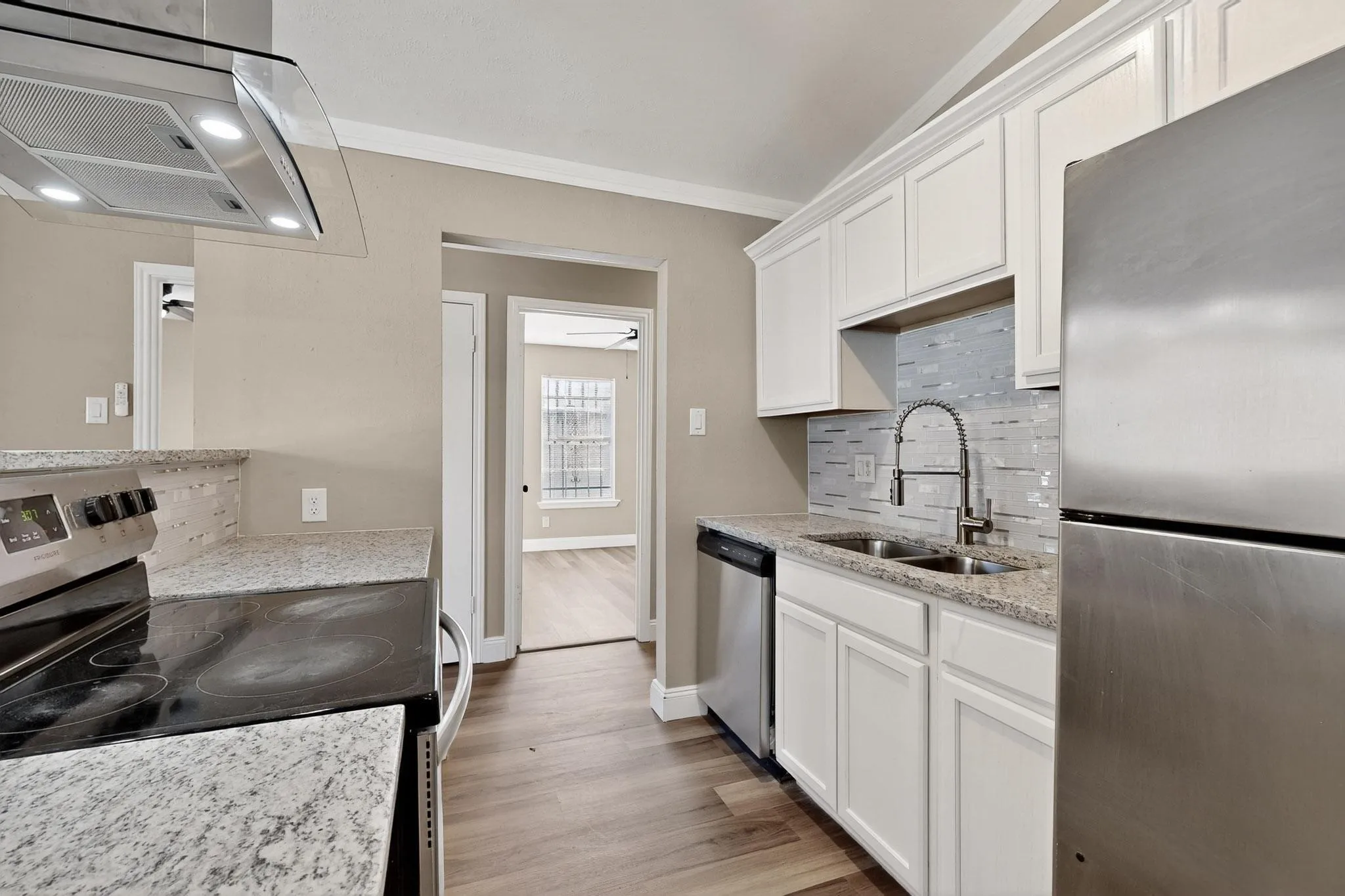 Kitchen featuring stainless steel appliances, exhaust hood, white cabinets, light stone counters, and crown molding