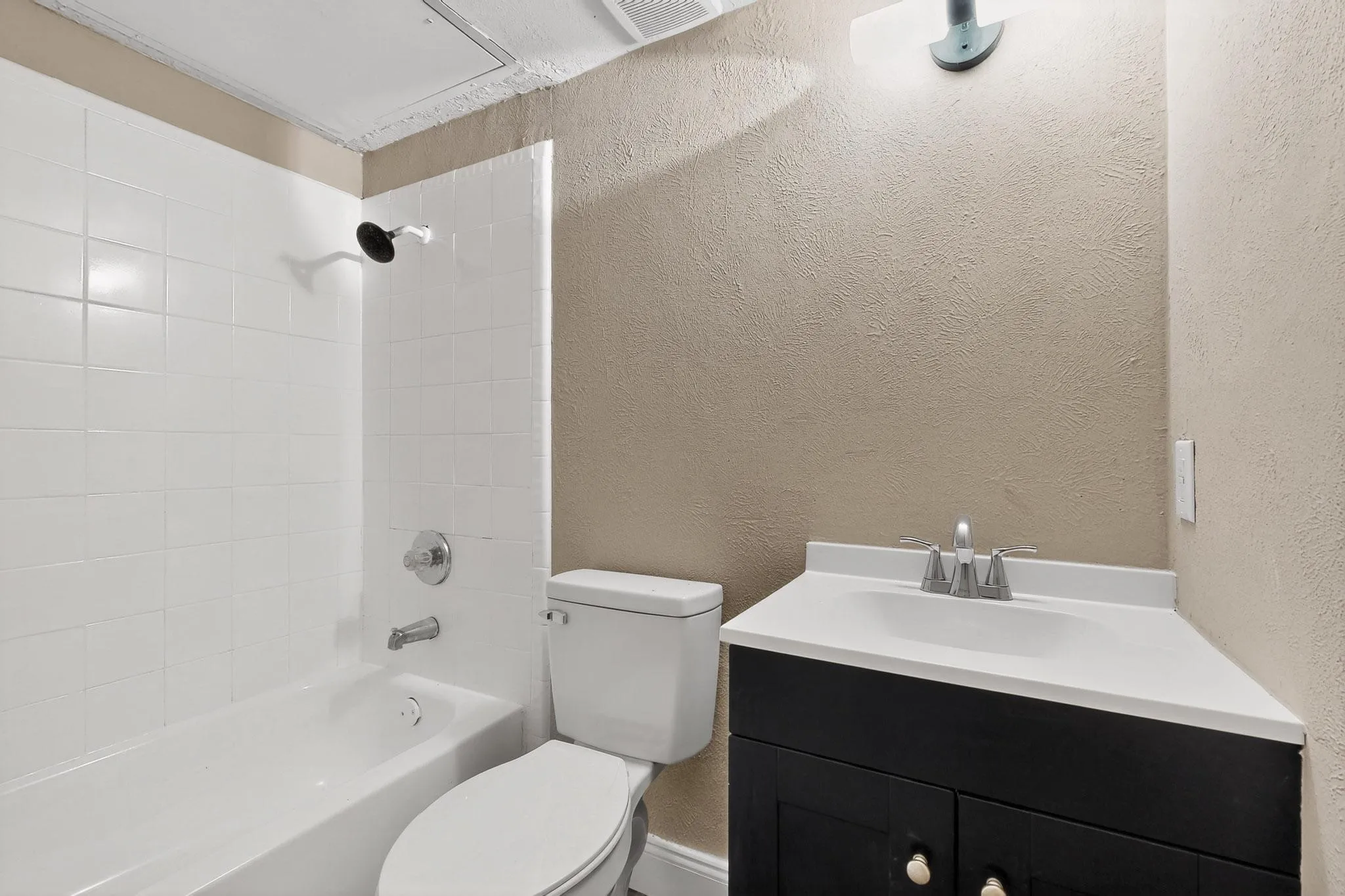 Bathroom with a textured wall, vanity, and shower / bath combination