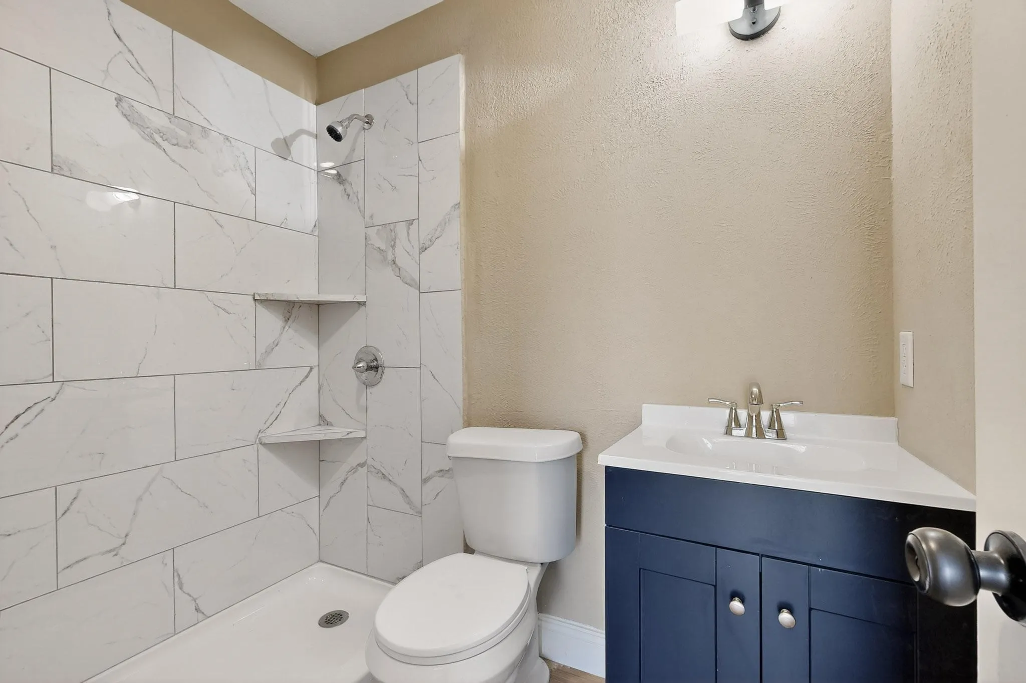 Bathroom featuring vanity, tiled shower, and a textured wall