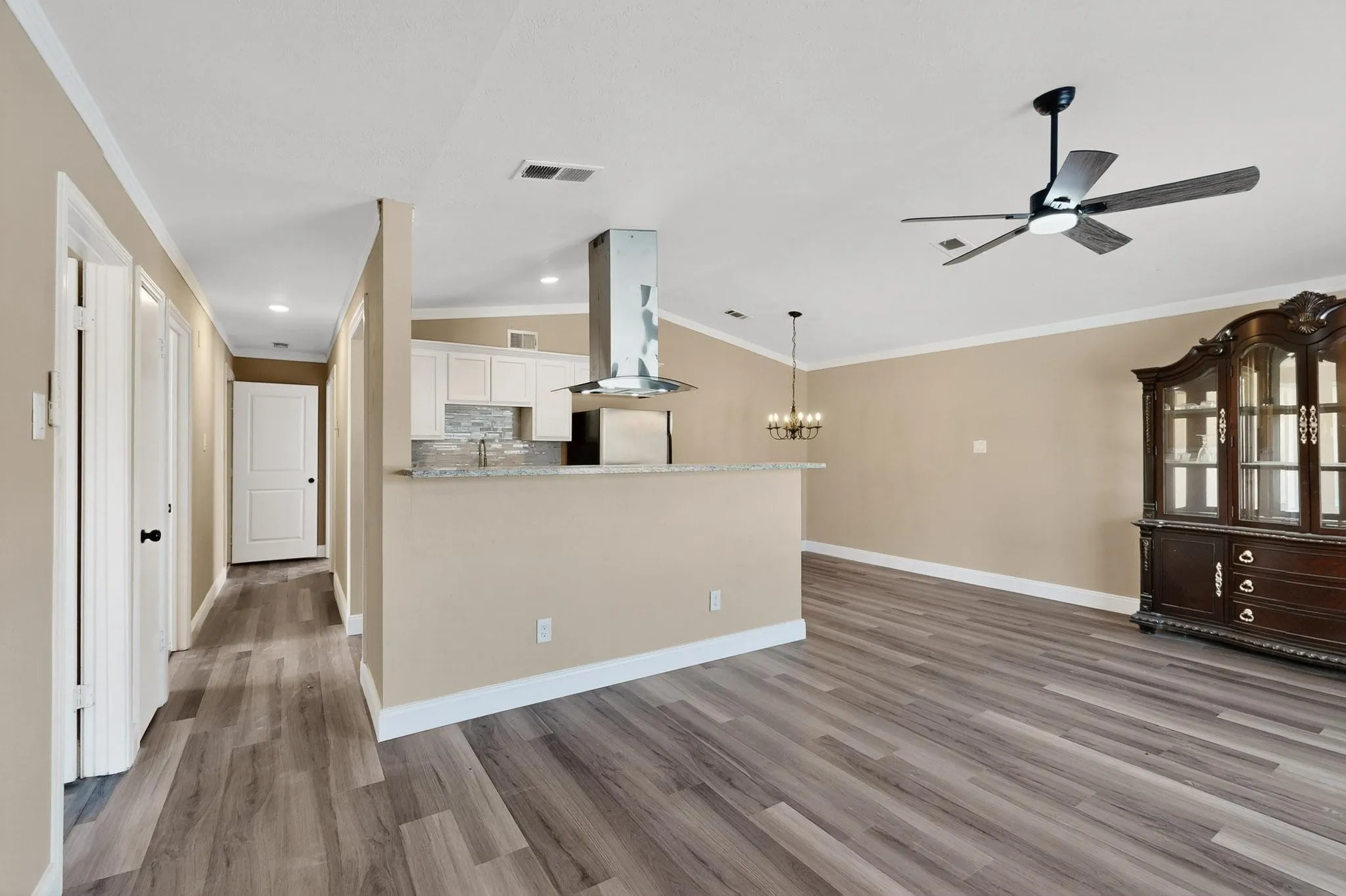 Kitchen featuring backsplash, island exhaust hood, crown molding, white cabinets, and wood finished floors