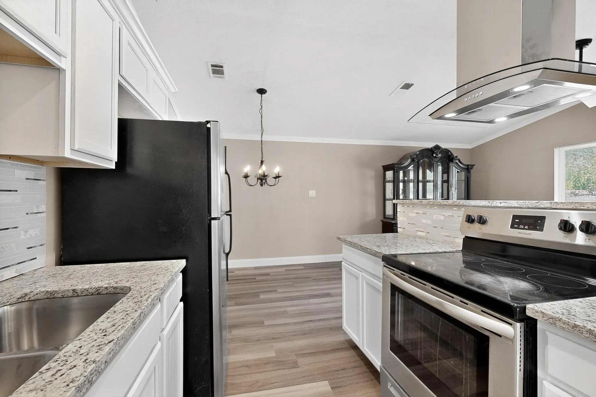 Kitchen with stainless steel appliances, white cabinetry, range hood, ornamental molding, and a chandelier