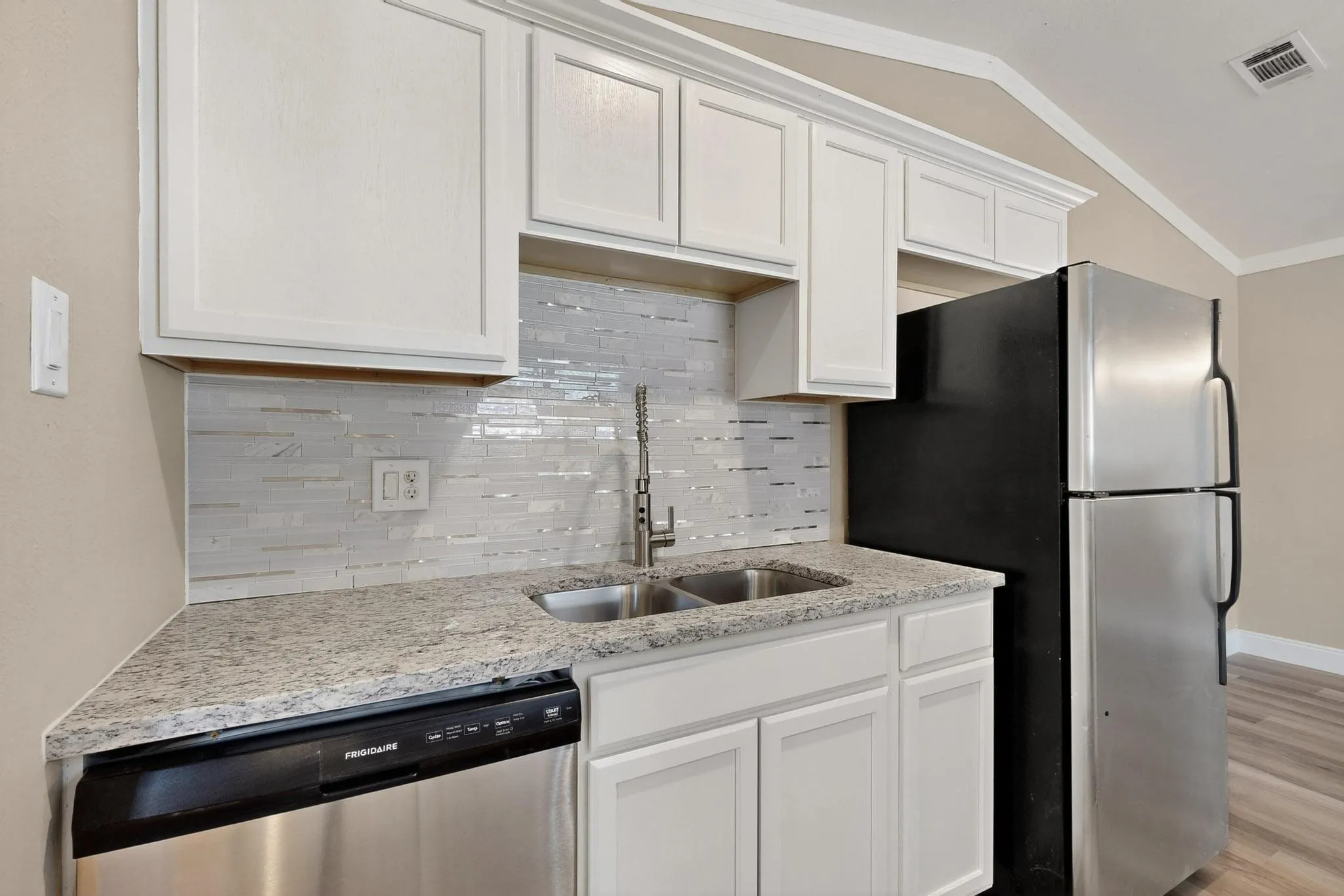 Kitchen featuring decorative backsplash, appliances with stainless steel finishes, white cabinetry, ornamental molding, and vaulted ceiling