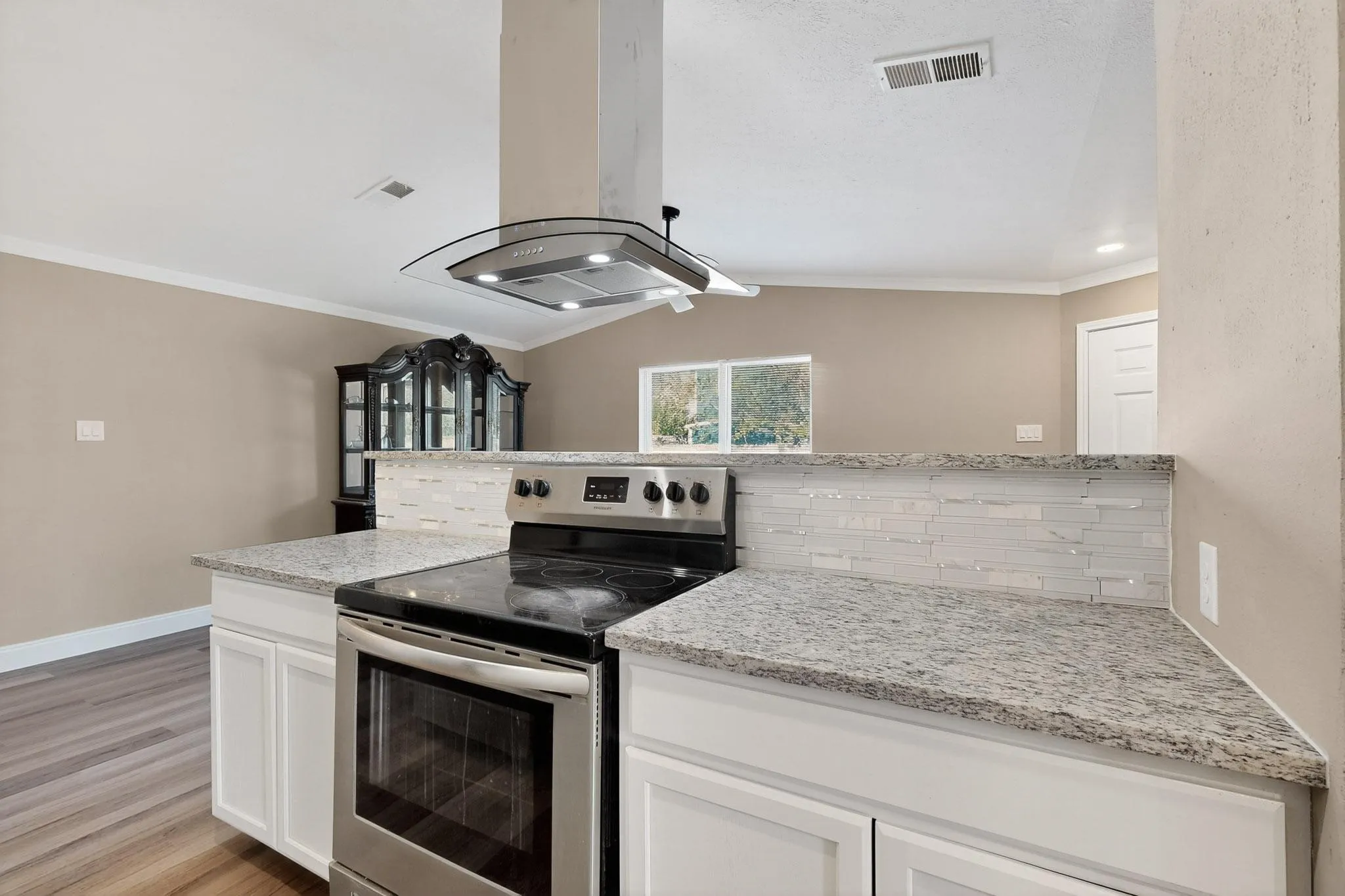 Kitchen with stainless steel electric range, white cabinetry, backsplash, ornamental molding, and island exhaust hood