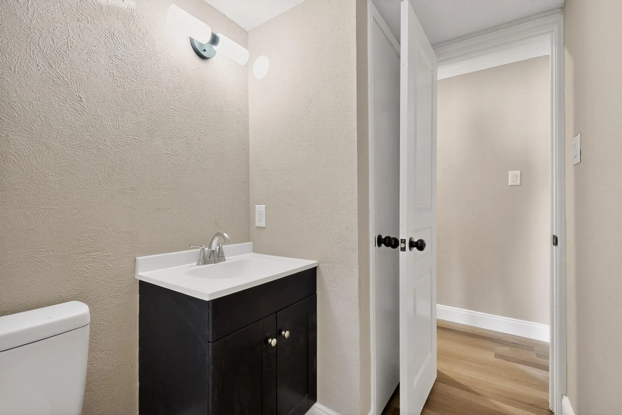 Half bathroom featuring vanity, light wood-style flooring, and a textured wall