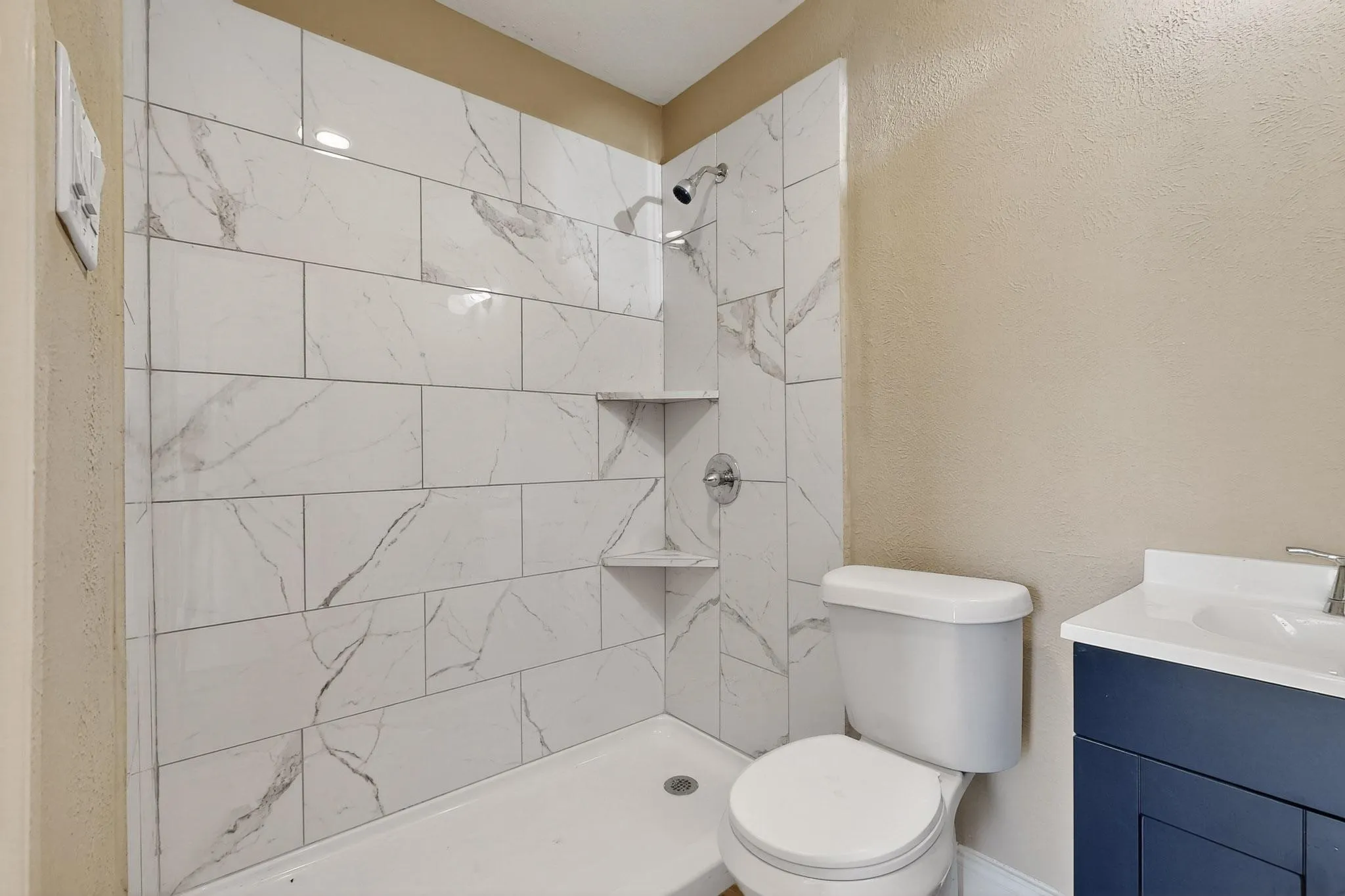 Full bath with a textured wall, tiled shower, and vanity