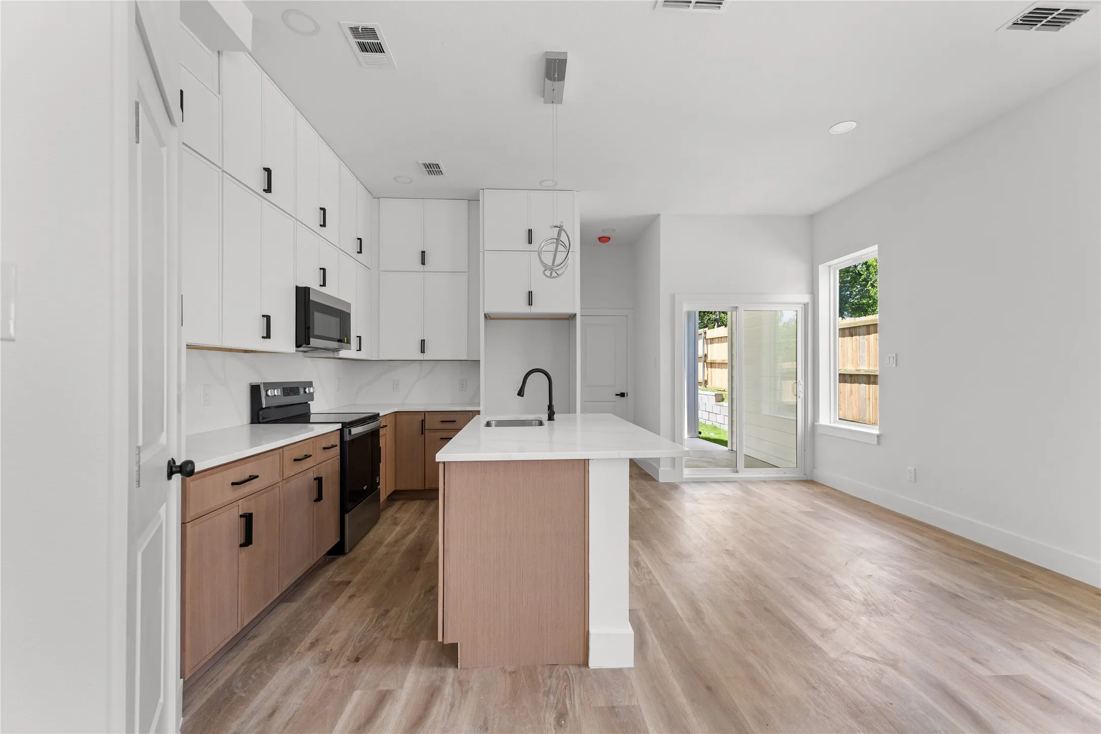 Modern kitchen featuring two-tone cabinetry with white upper and wood-finish lower cabinets, black hardware, an island with a sink and a gooseneck faucet, and stainless steel appliances