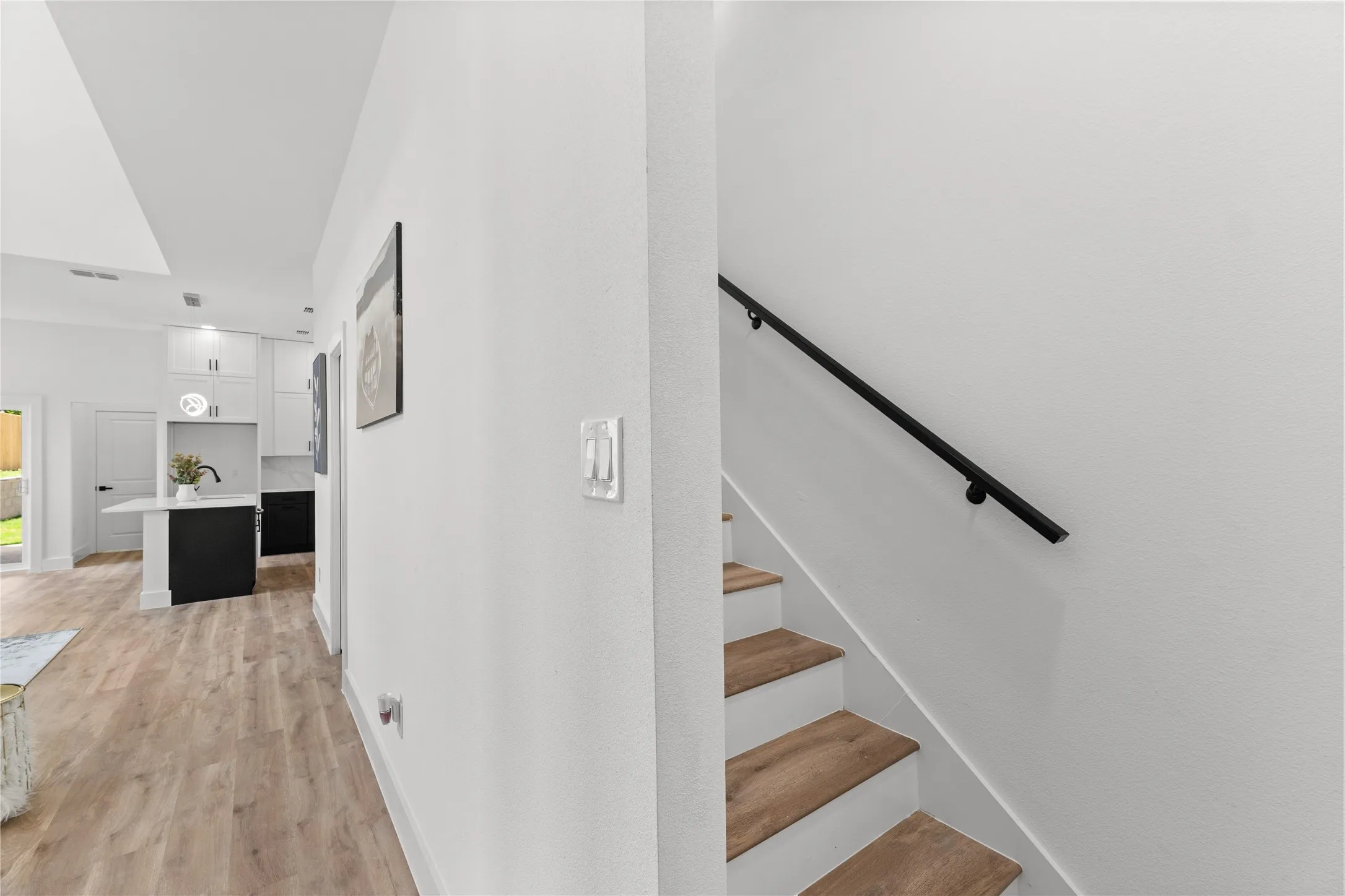 Modern interior featuring light wood-finish flooring, white walls, and a contemporary black handrail
