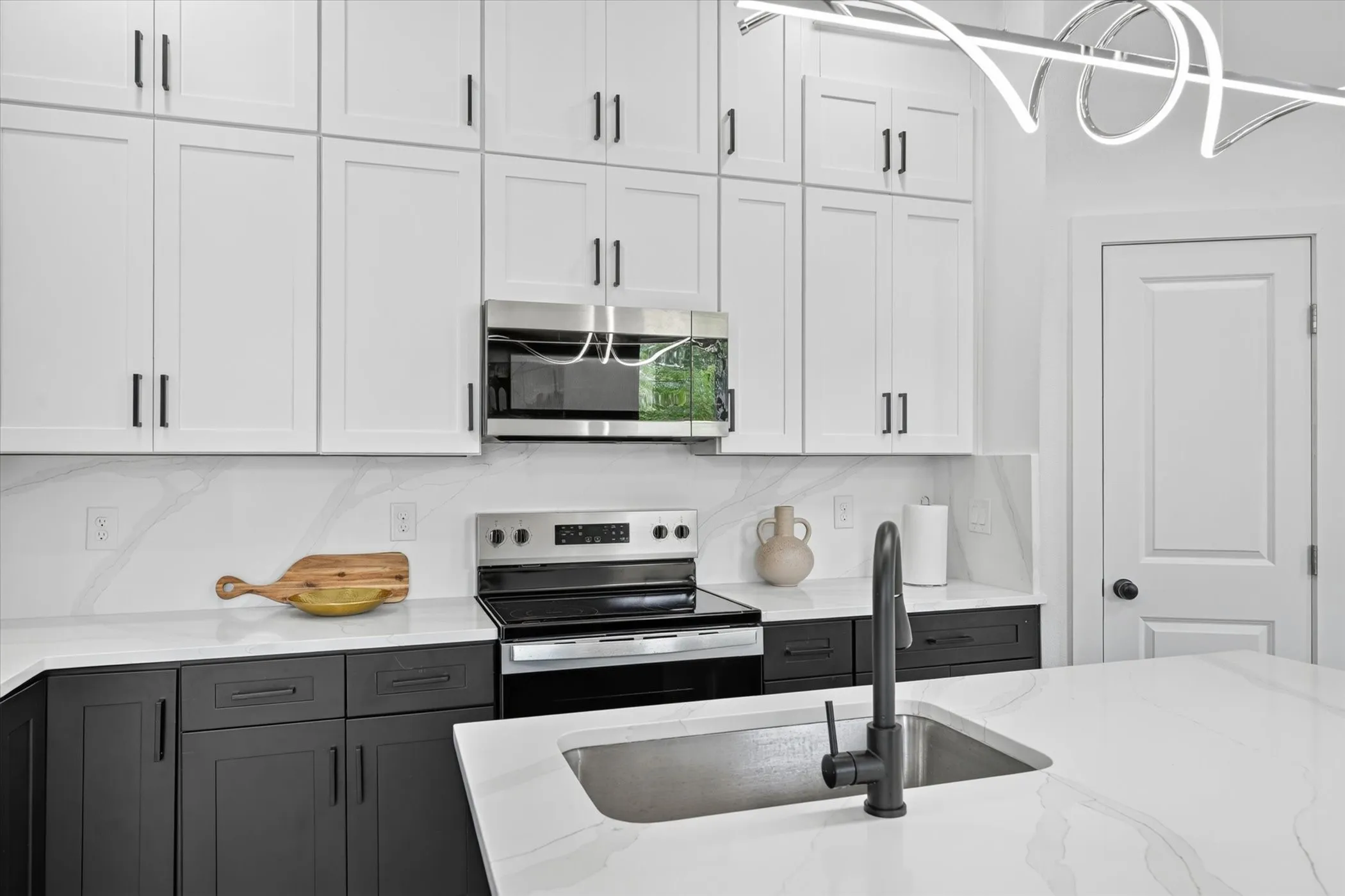 Modern kitchen featuring two-tone cabinetry with matte black hardware, white countertops, and a white tile backsplash