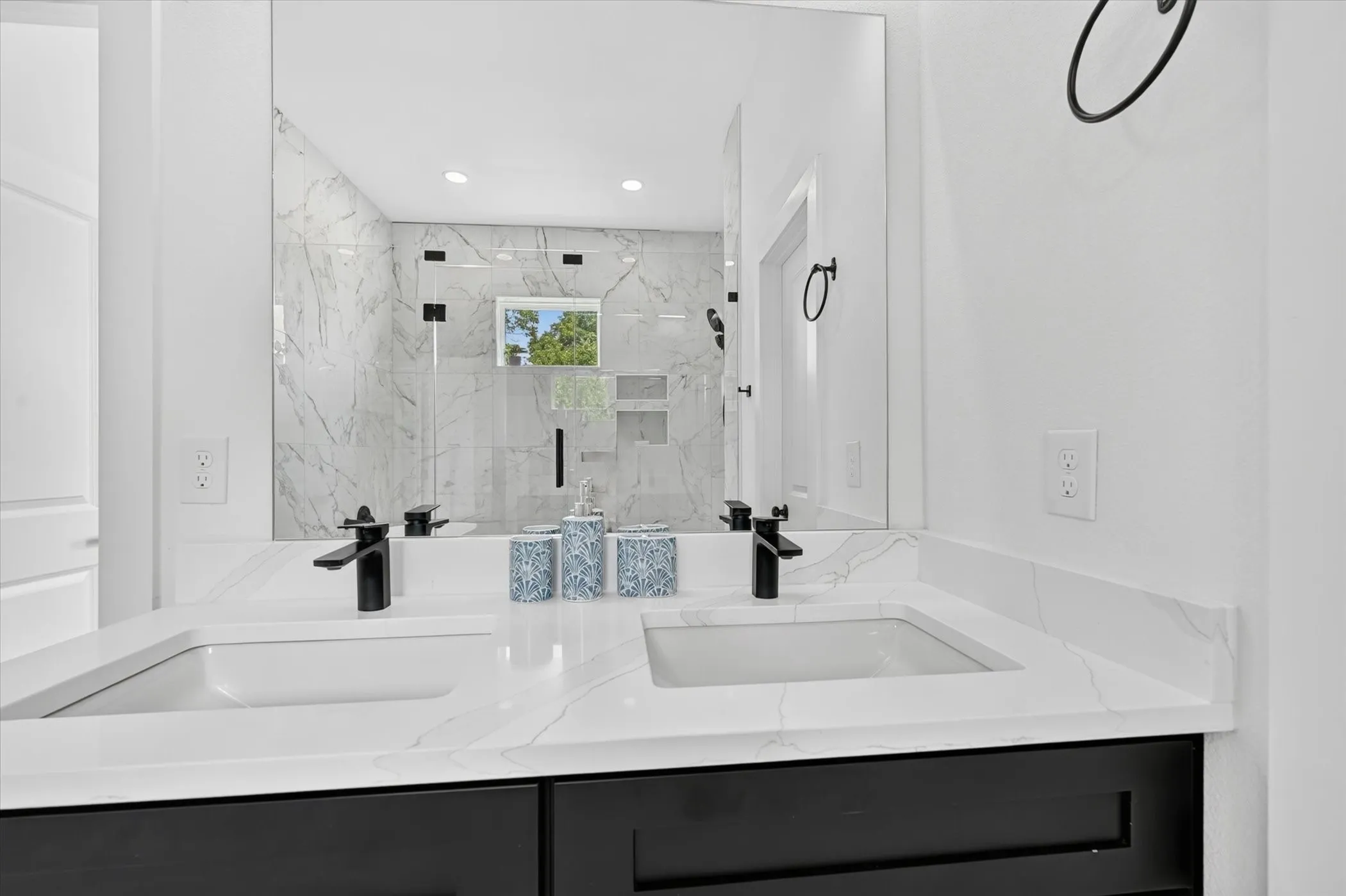 Double vanity featuring dual integrated sinks, white countertops with subtle veining, matte black faucets, and a large unframed mirror
