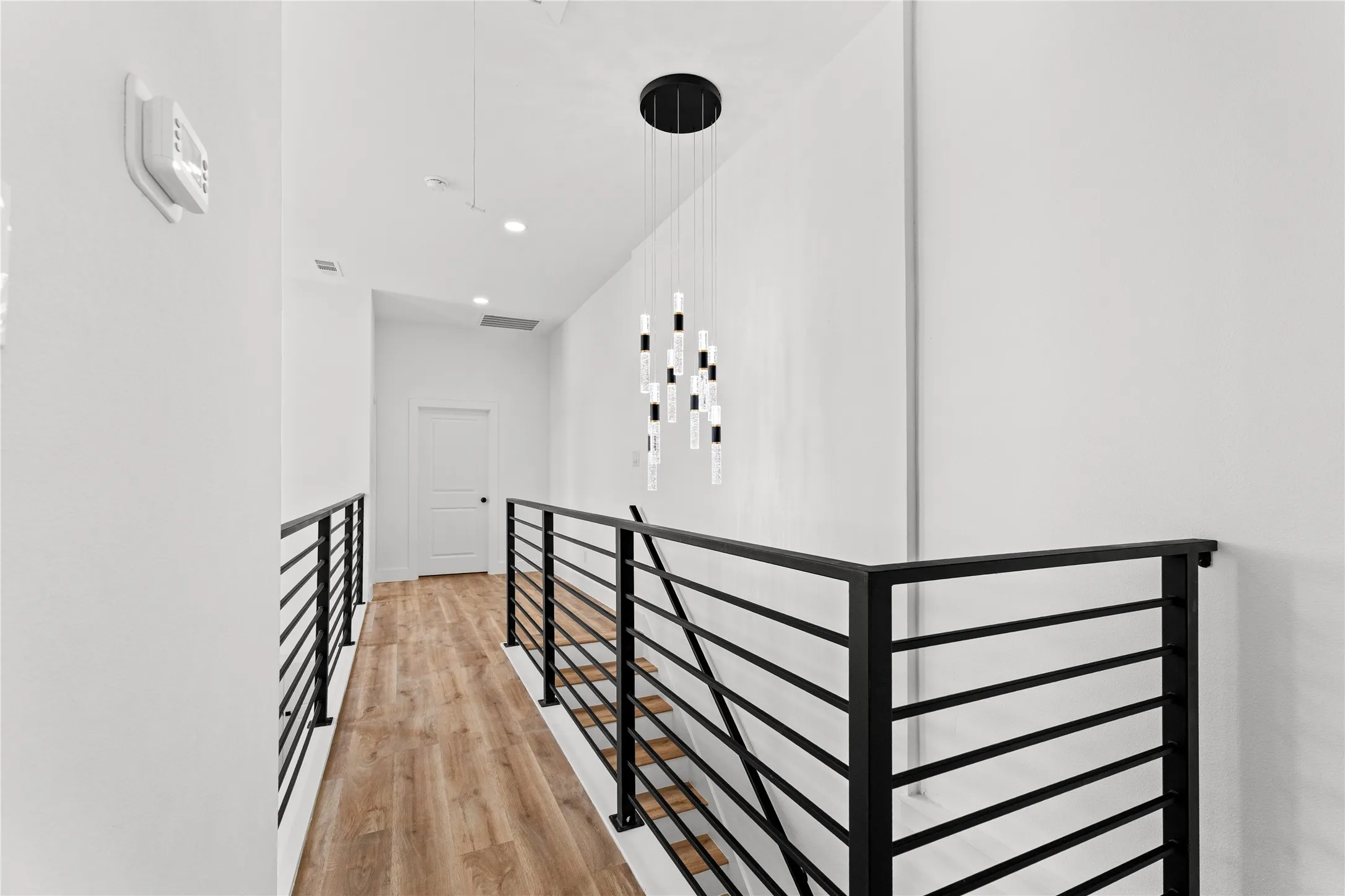 Hallway featuring wood-finish flooring, a contemporary chandelier, recessed lighting, and modern black horizontal railing
