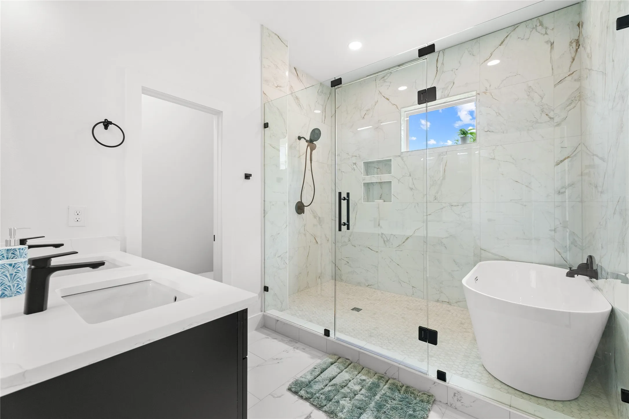 Modern bathroom featuring a dual vanity with undermount sinks and matte black faucets, a glass-enclosed shower with full-height tile surround, and a freestanding soaking tub