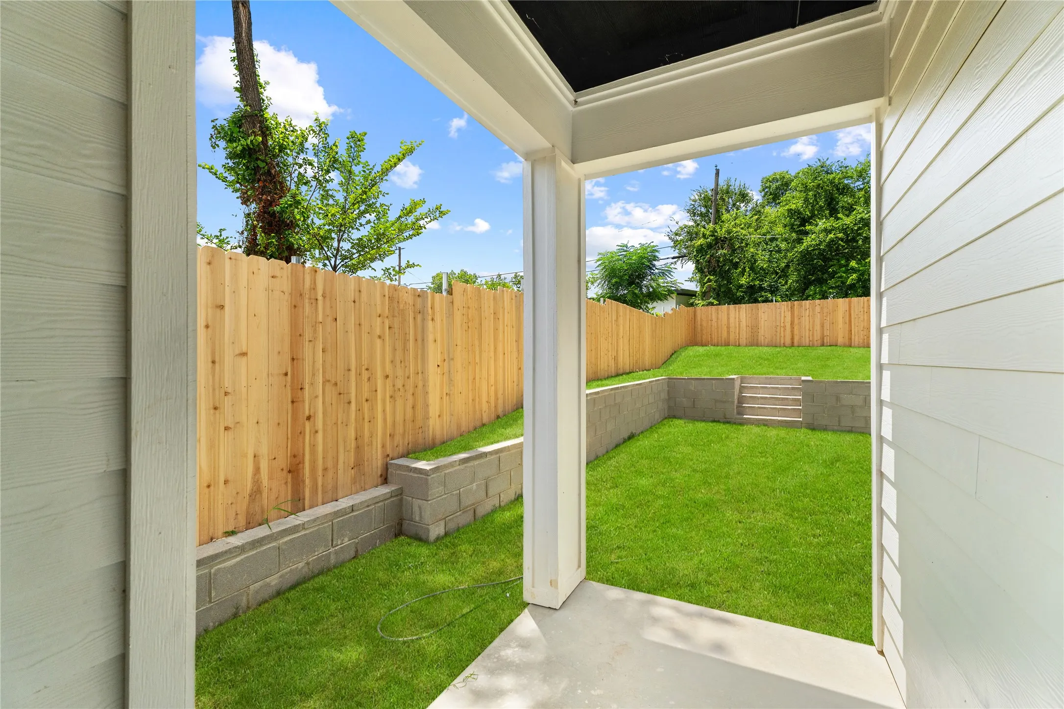 Tiered backyard with a manicured lawn, concrete block retaining walls, and a new privacy fence