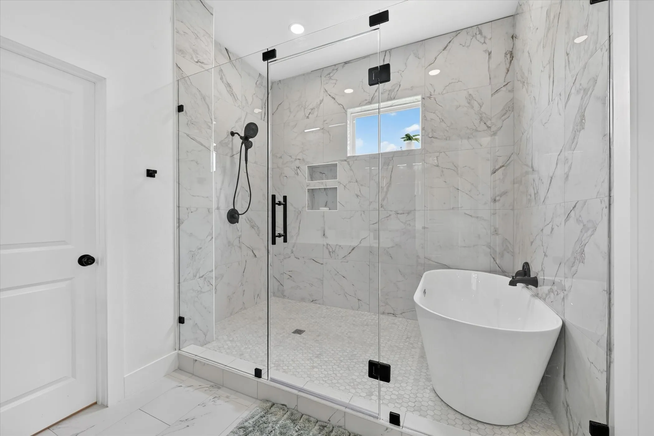 Spacious shower enclosure with glass panels, white marble-look tile, and matte black fixtures