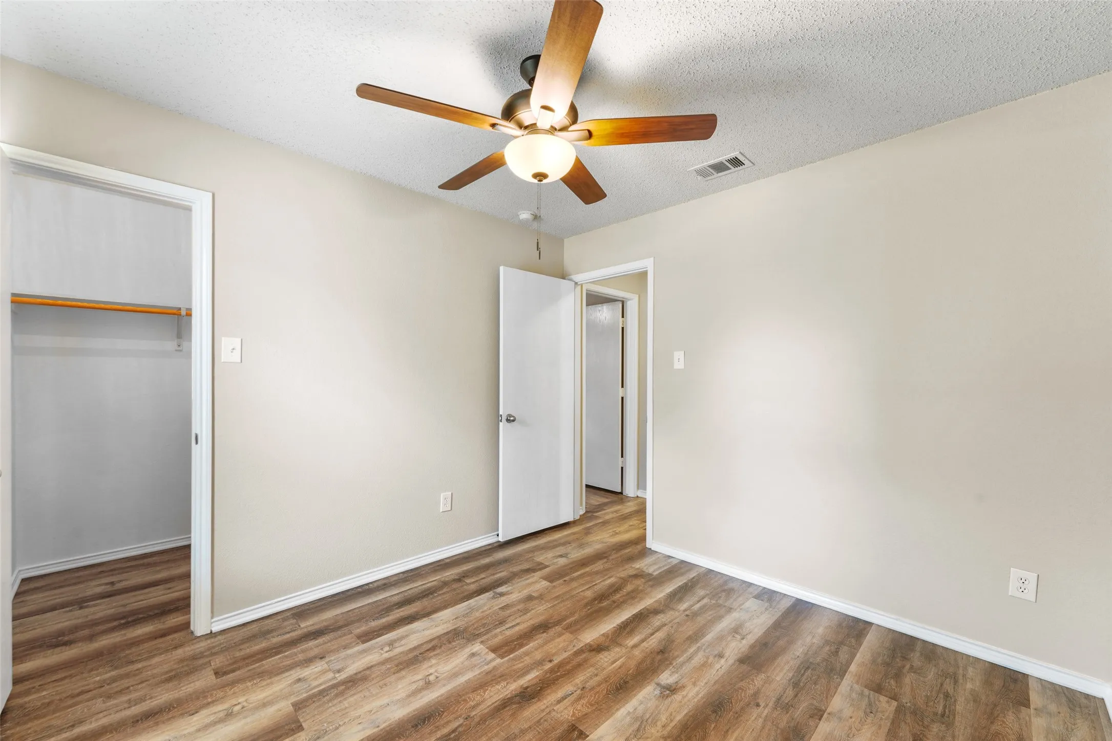Spacious room featuring wood-finish flooring, a contemporary ceiling fan with light fixture, neutral wall finishes, and a built-in closet with shelving