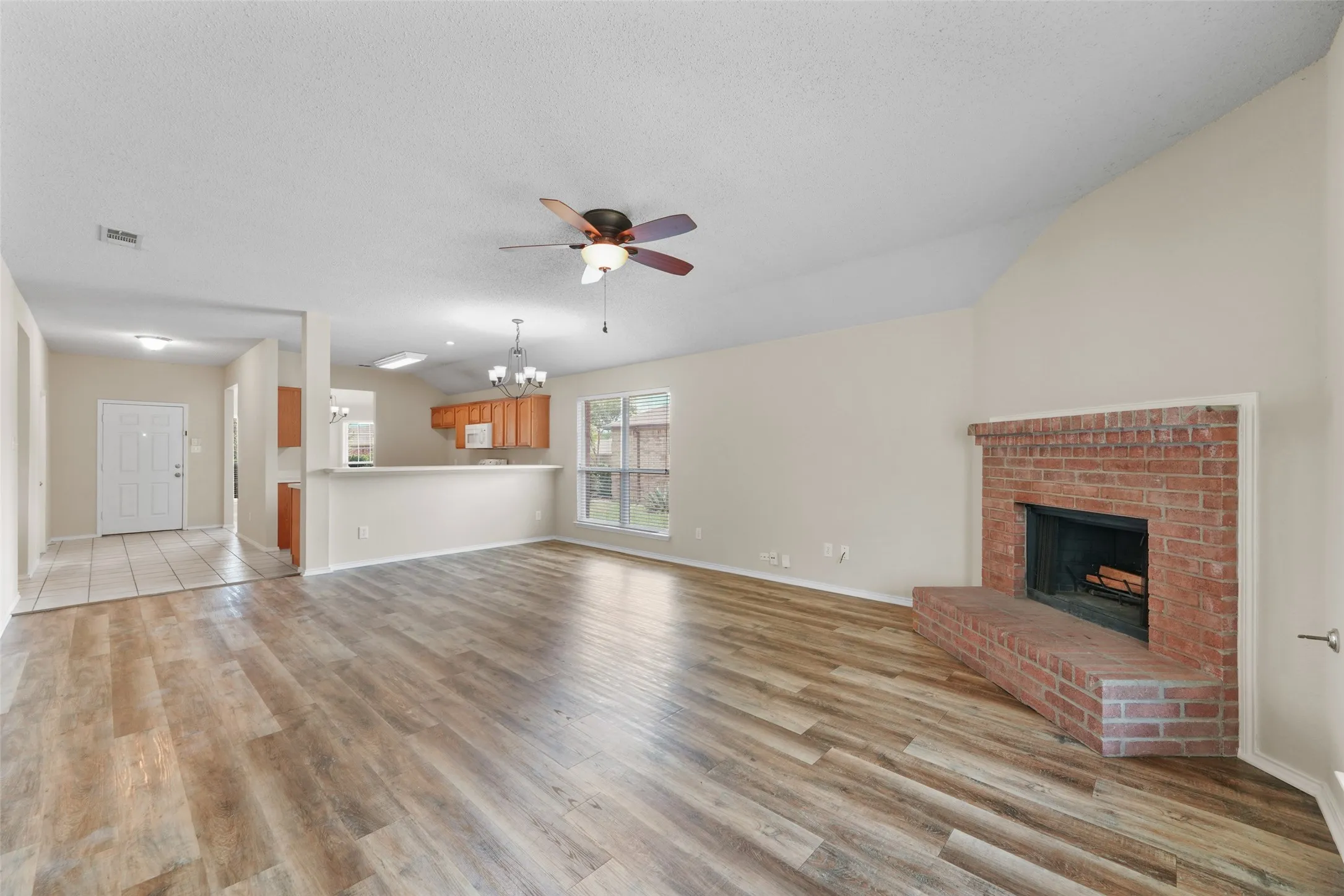 Expansive living area featuring wood-finish flooring, a vaulted ceiling, and a brick fireplace