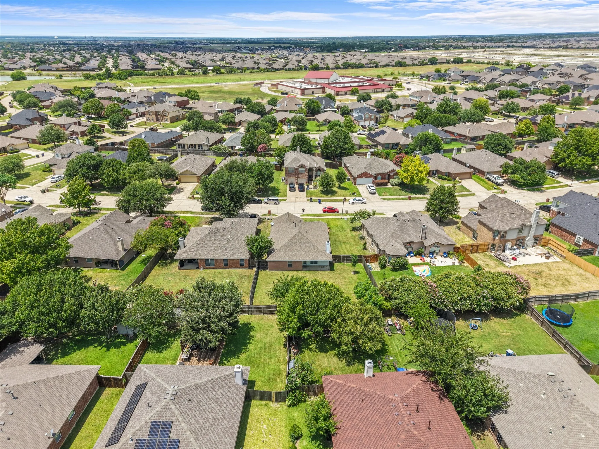 Aerial perspective of a residential neighborhood featuring numerous single-family homes with pitched roofs, mature trees, and manicured lawns