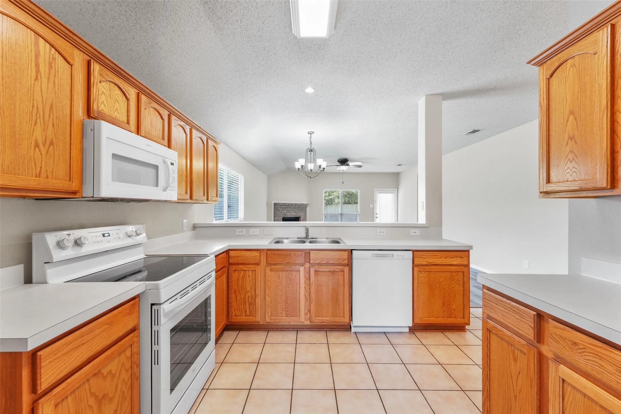 Kitchen featuring wood cabinetry, light countertops, tile flooring, and integrated white appliances including an electric range, microwave, and dishwasher