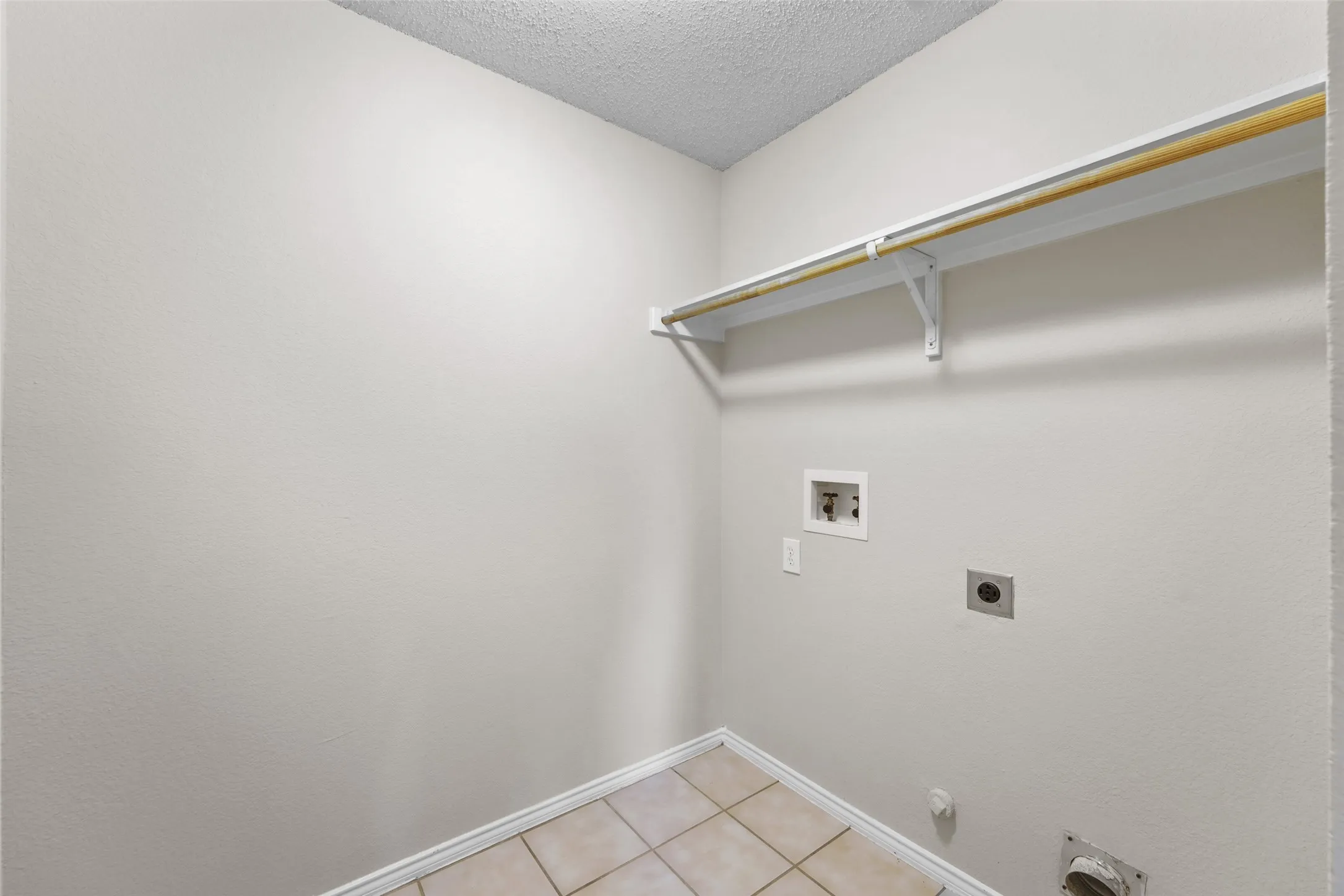 Dedicated laundry space featuring a neutral color palette, tile flooring, a built-in shelf, and a clothing rod
