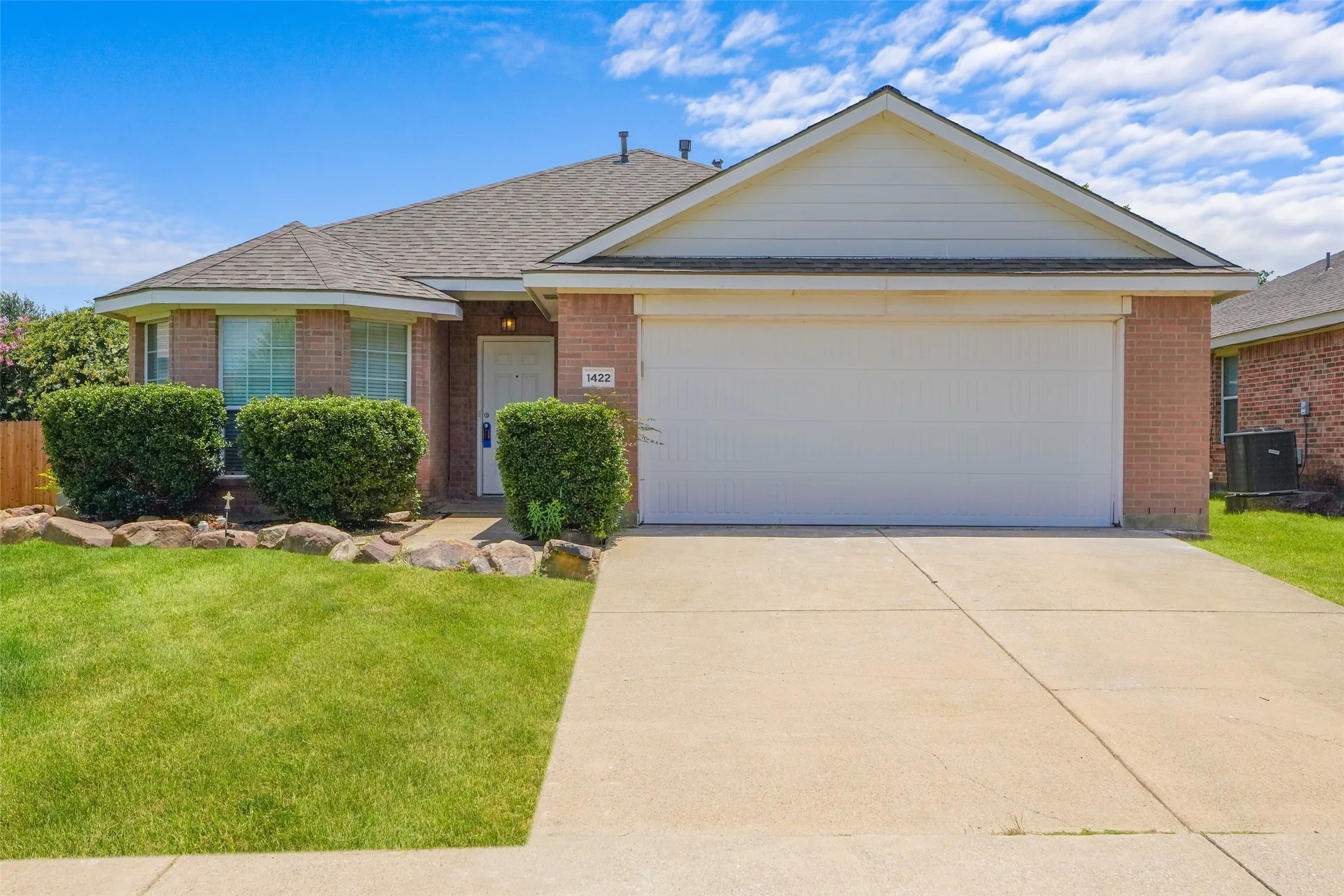 Brick exterior featuring a two-car garage, concrete driveway, and a front lawn