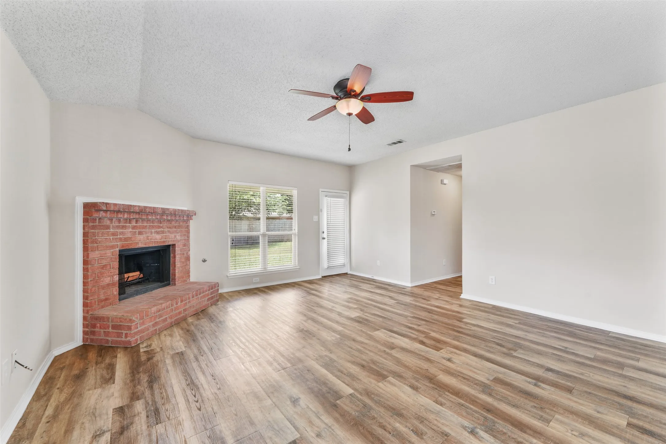 Spacious living area featuring wood-finish flooring, a red brick fireplace, and a ceiling fan