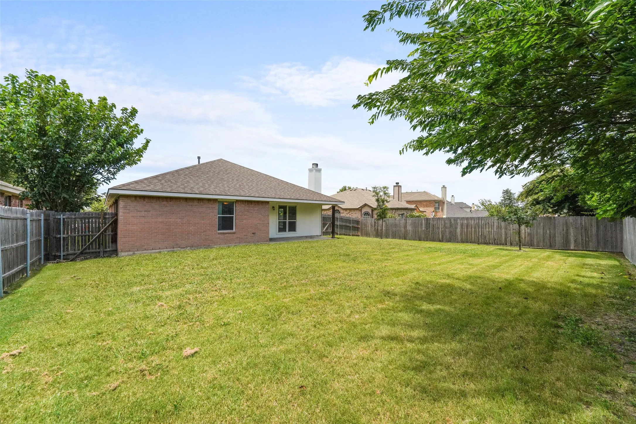 Expansive backyard featuring a lush lawn, privacy fencing, and mature trees