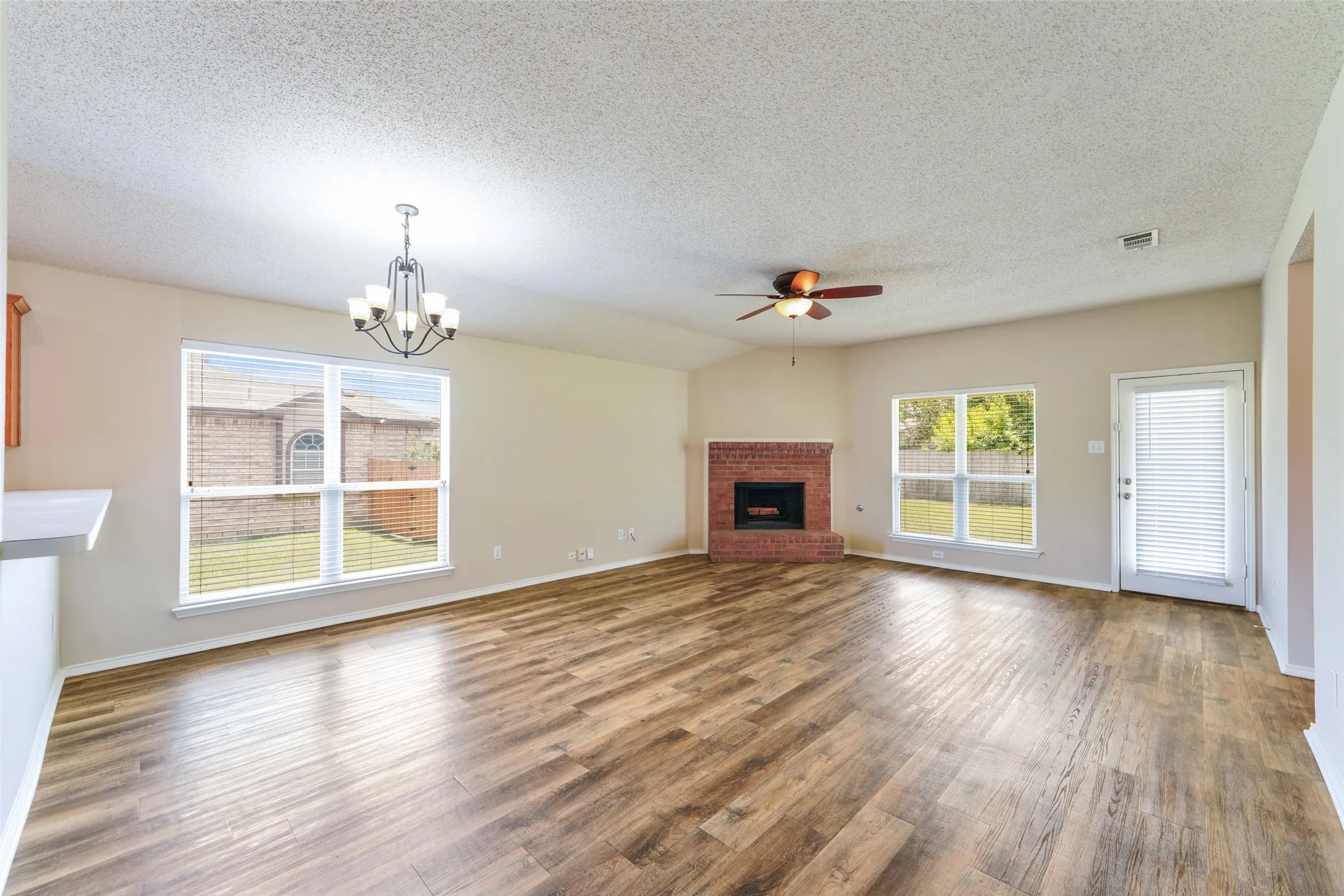 Spacious living area featuring wood-finish flooring, a brick fireplace, a ceiling fan, and multiple windows with blinds