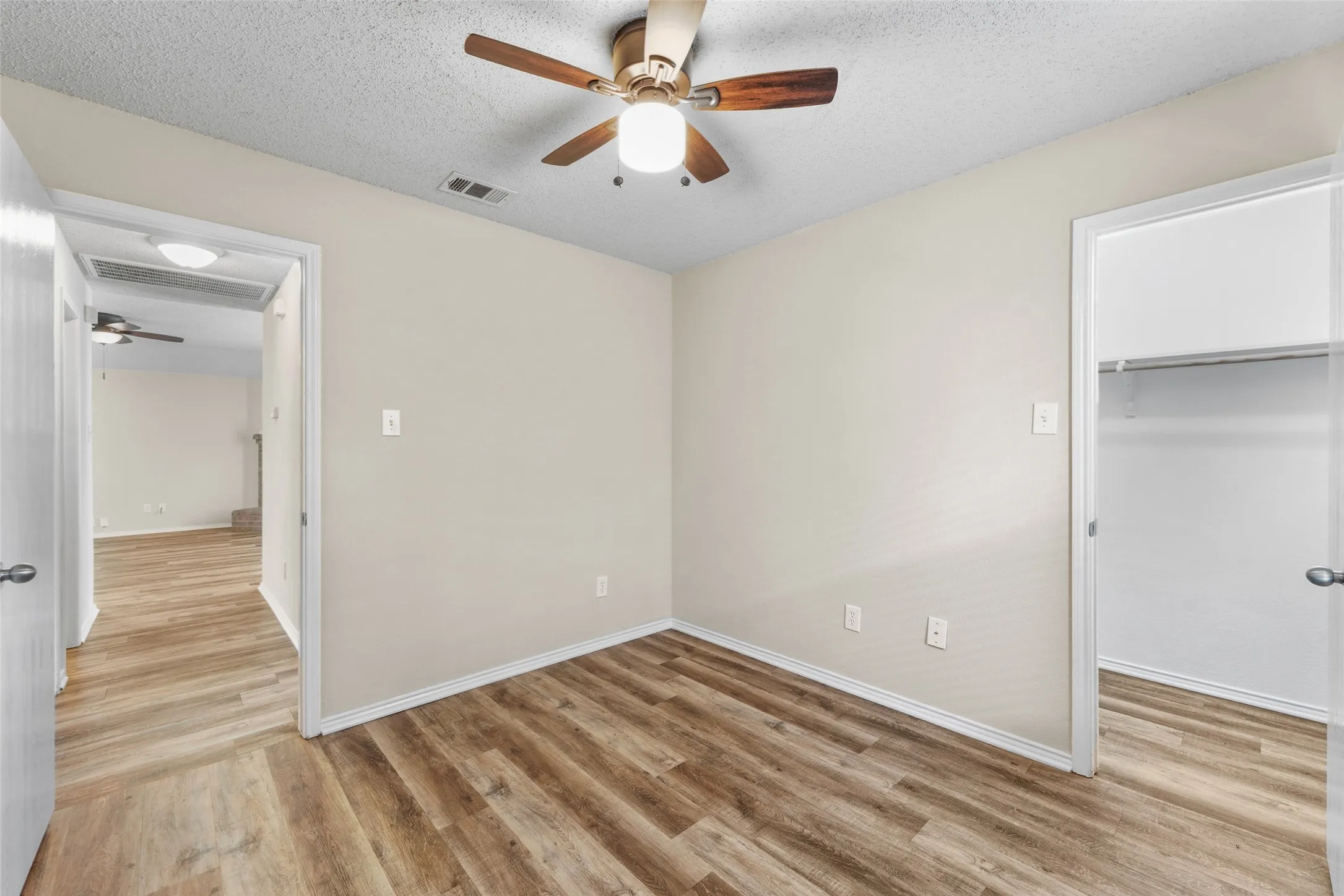 Interior room featuring wood-finish flooring, light-toned wall paint, a ceiling fan with integrated lighting, and a closet with a hanging rod