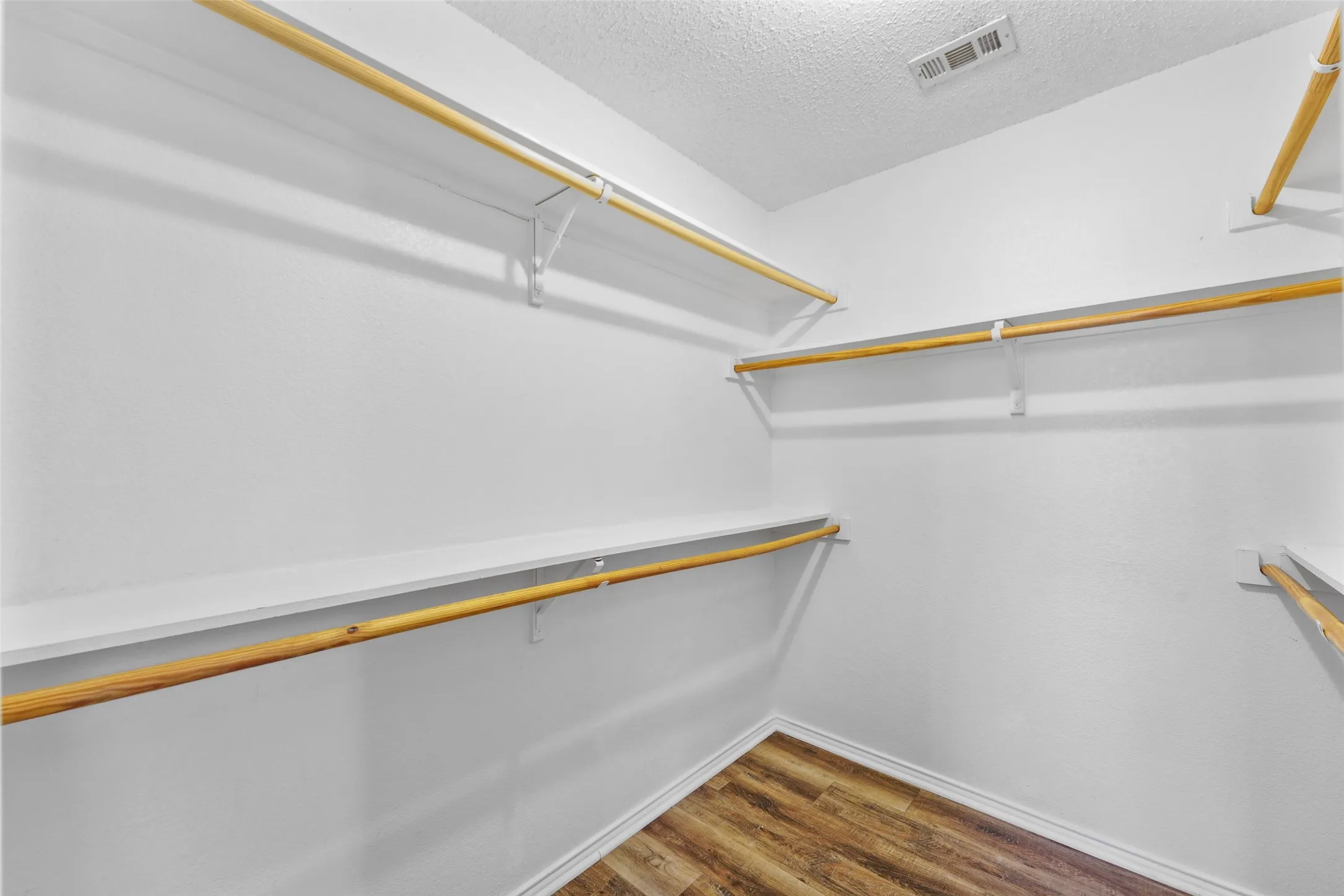 Walk-in closet featuring white walls, textured ceiling, wood-finish flooring, and multiple levels of shelving and hanging rods