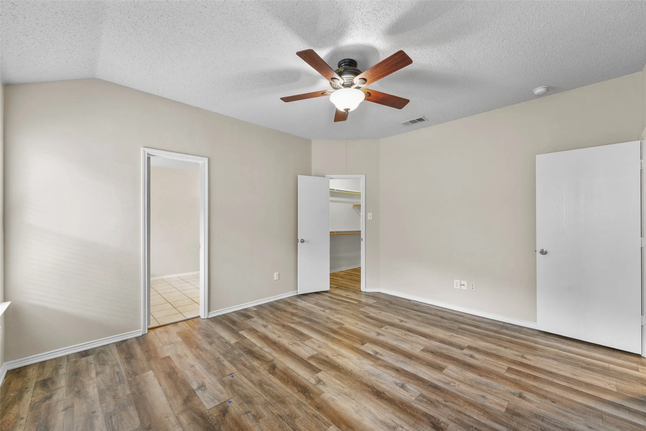 Room featuring wood-finish flooring, a ceiling fan with integrated lighting, vaulted ceilings, and neutral wall tones
