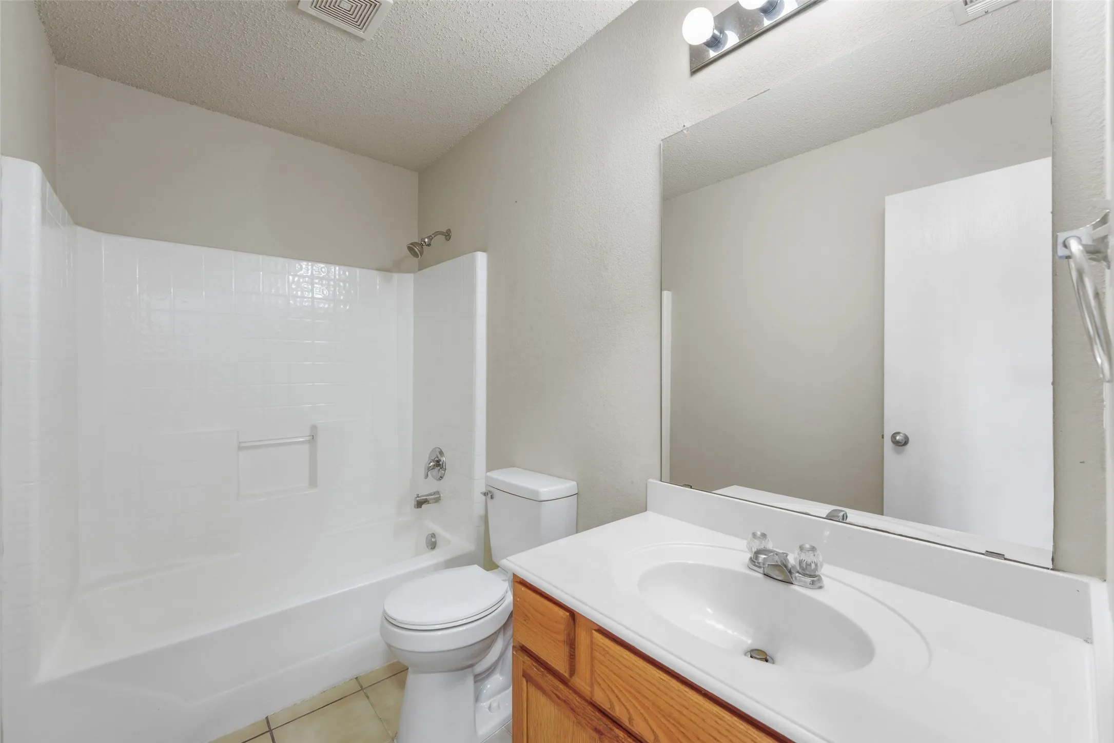 Bathroom featuring a tub/shower combination with white surround, a white toilet, and a vanity with a white countertop and wood-finish cabinetry