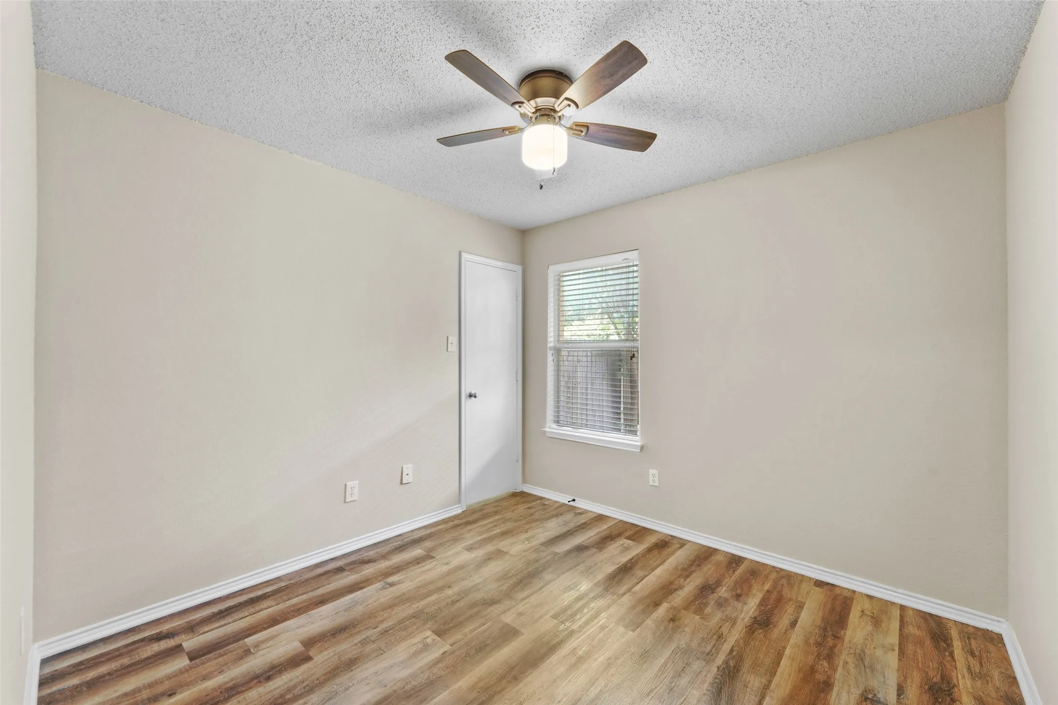 Room featuring wood-finish flooring, a ceiling fan with integrated lighting, a single window with blinds, and light-toned wall paint