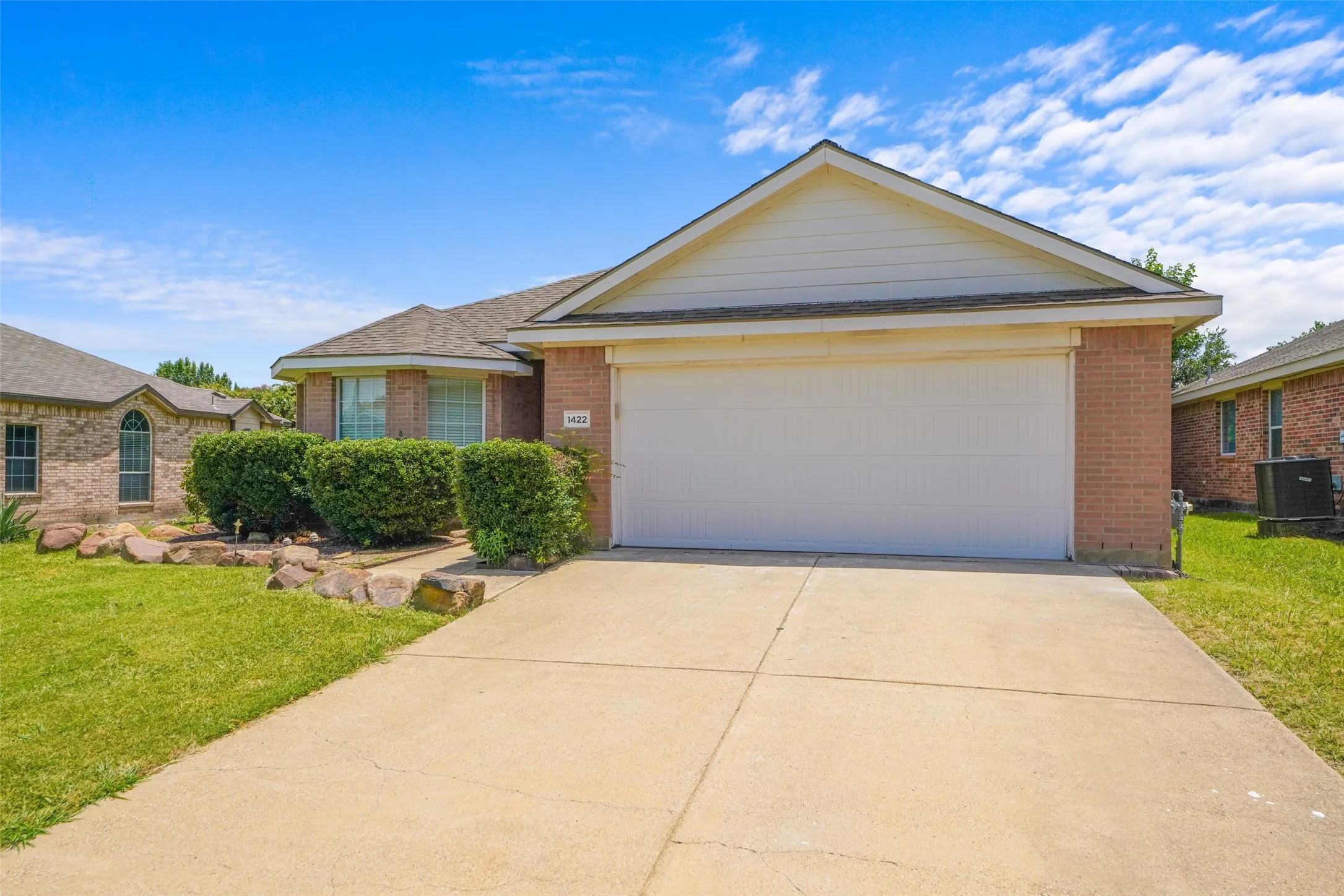 Brick exterior featuring a two-car garage, concrete driveway, and established shrubbery